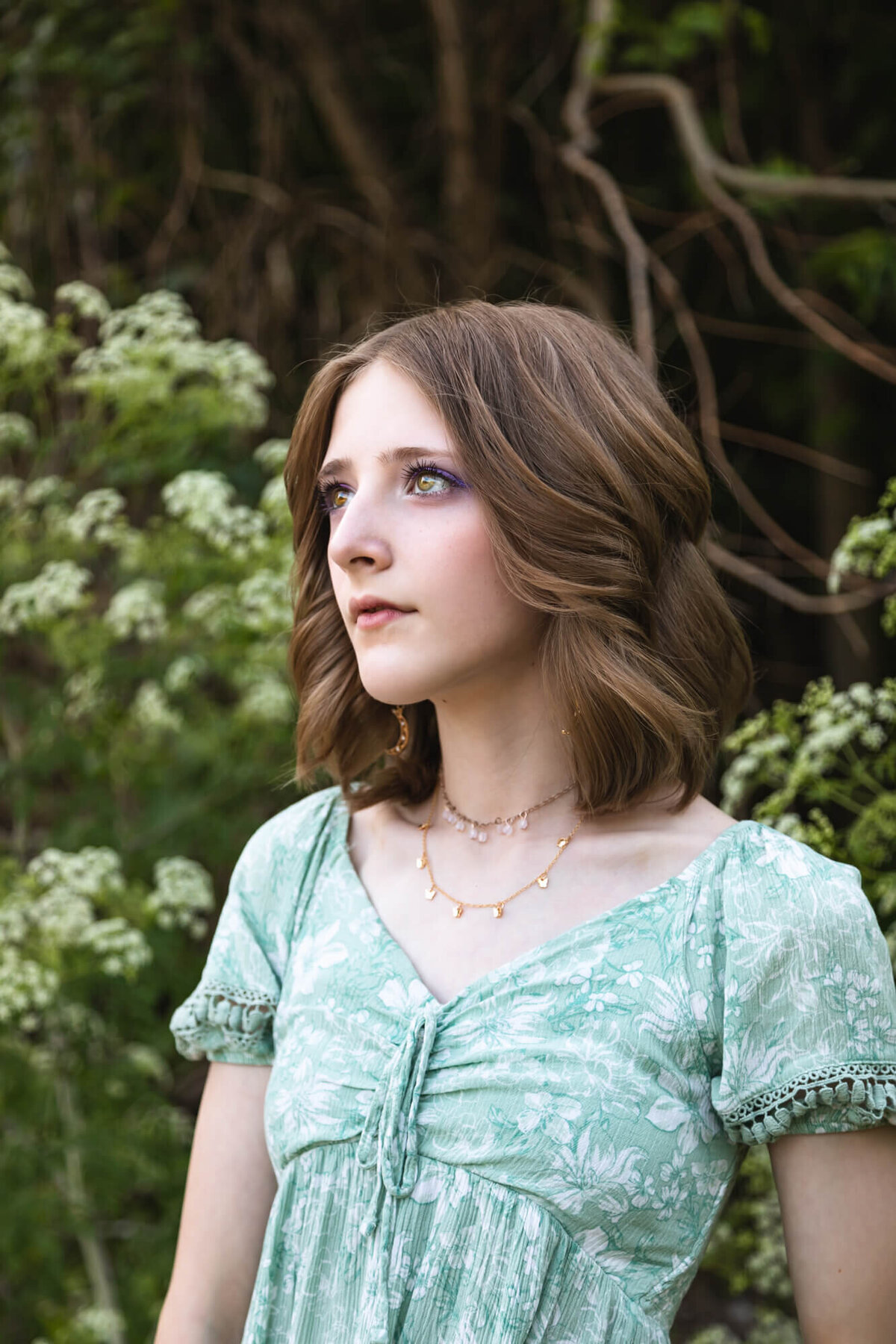 Striking portrait of a young teen girl with bobbed hair wearing a green floral dress in front of white flowers. Captured by Springfield, MO teen photographer Dynae Levingston.