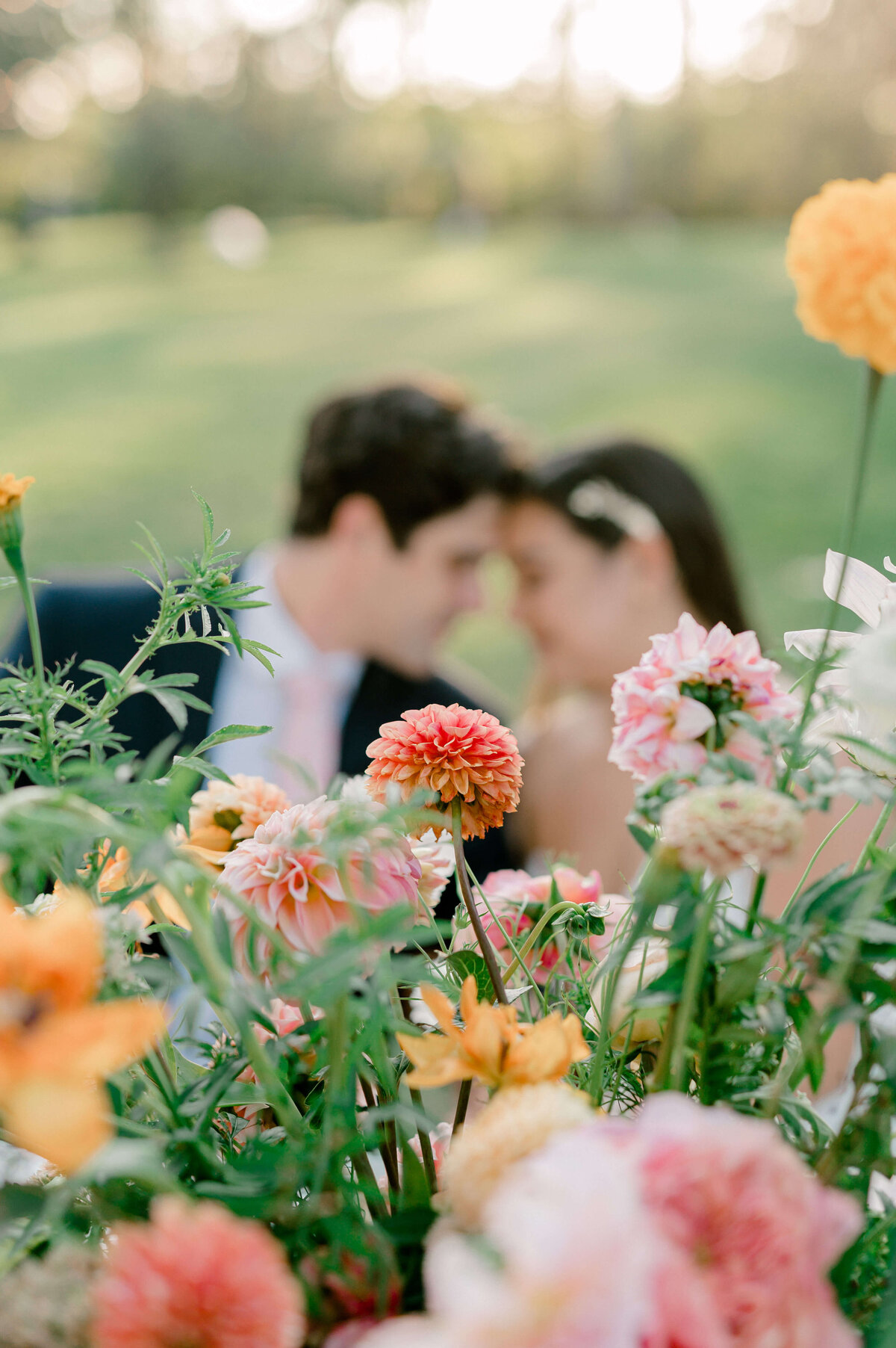 Couple resting forehead to forehead in the background with peach colored flowers in the foreground.