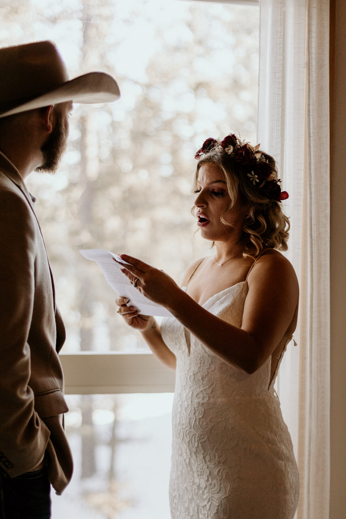 bride and groom exchanging personal vows in front of a window in a cabin