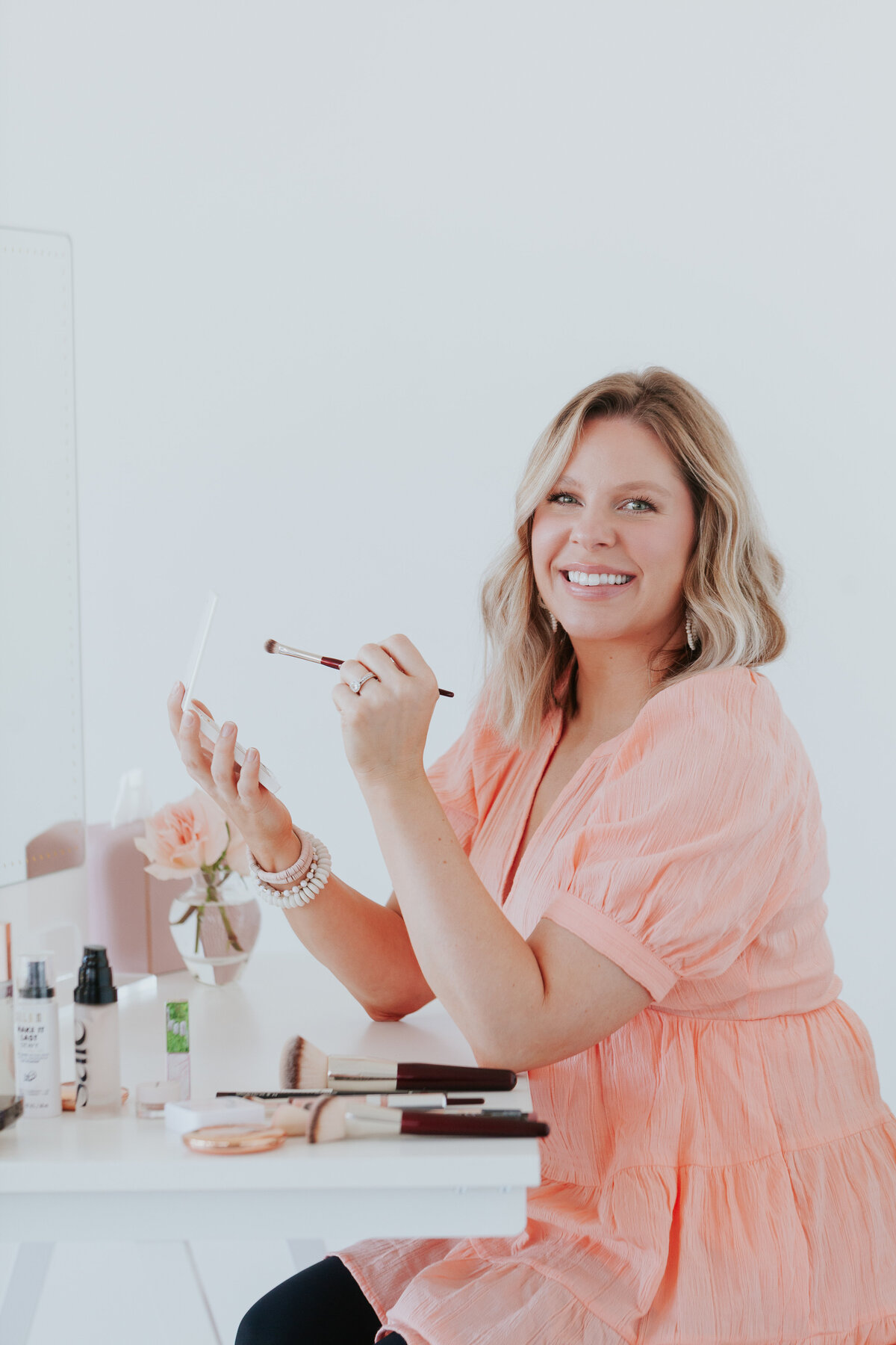 portrait-orientation-photo-makeup-artist-seated-at-vanitywith-makeup-and-brushes-for-brand-session-the-frame-charlotte
