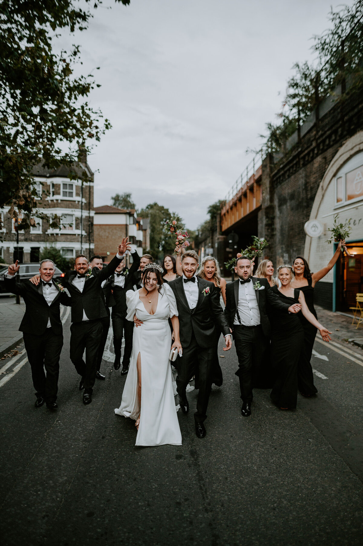A bride and groom walk down the train bridges in Brixton followed by their wedding party after their speeches at 100 Barrington.