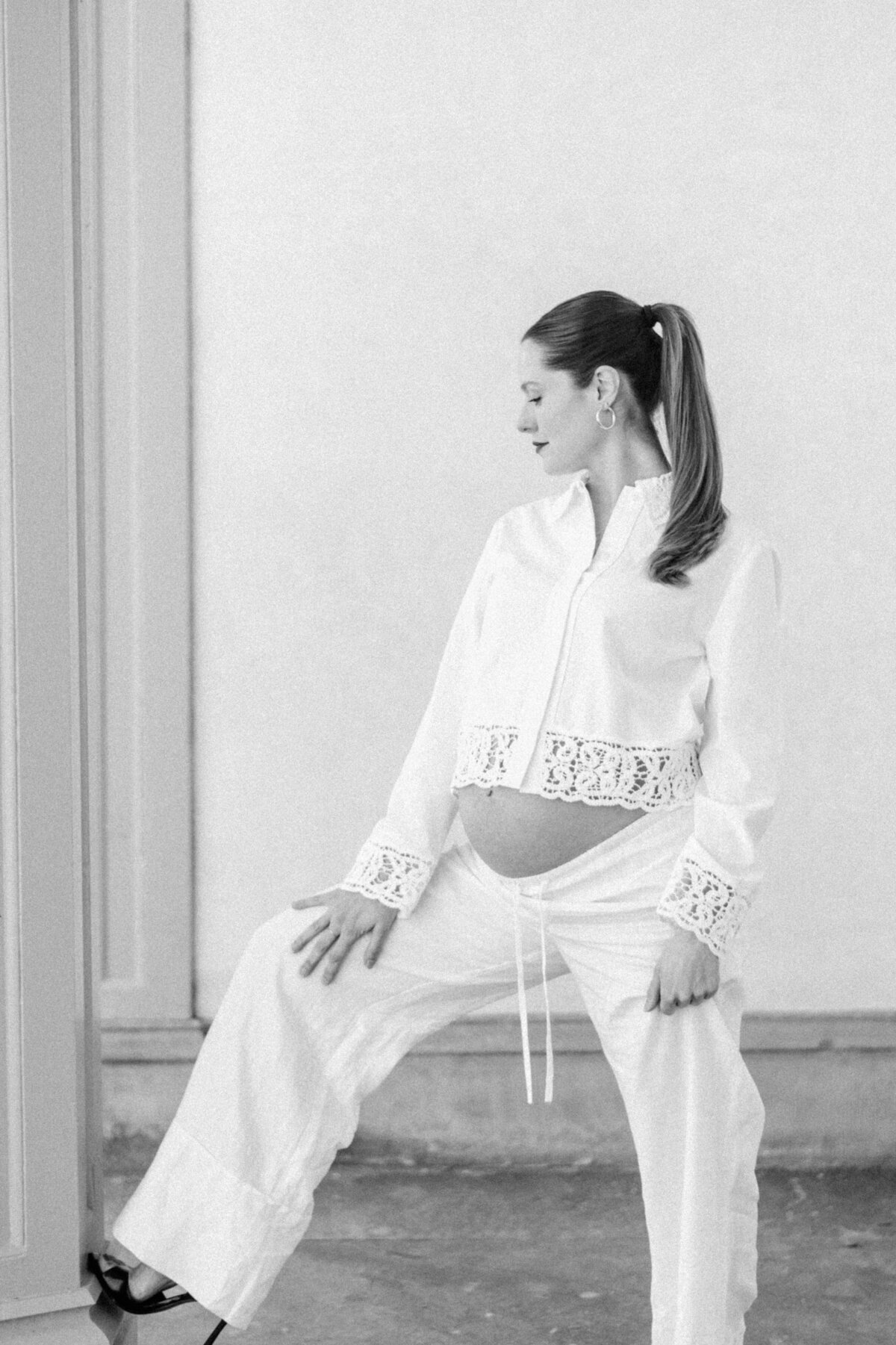Editorial black-and-white maternity portrait of a poised mother-to-be in heels, framed by architectural columns