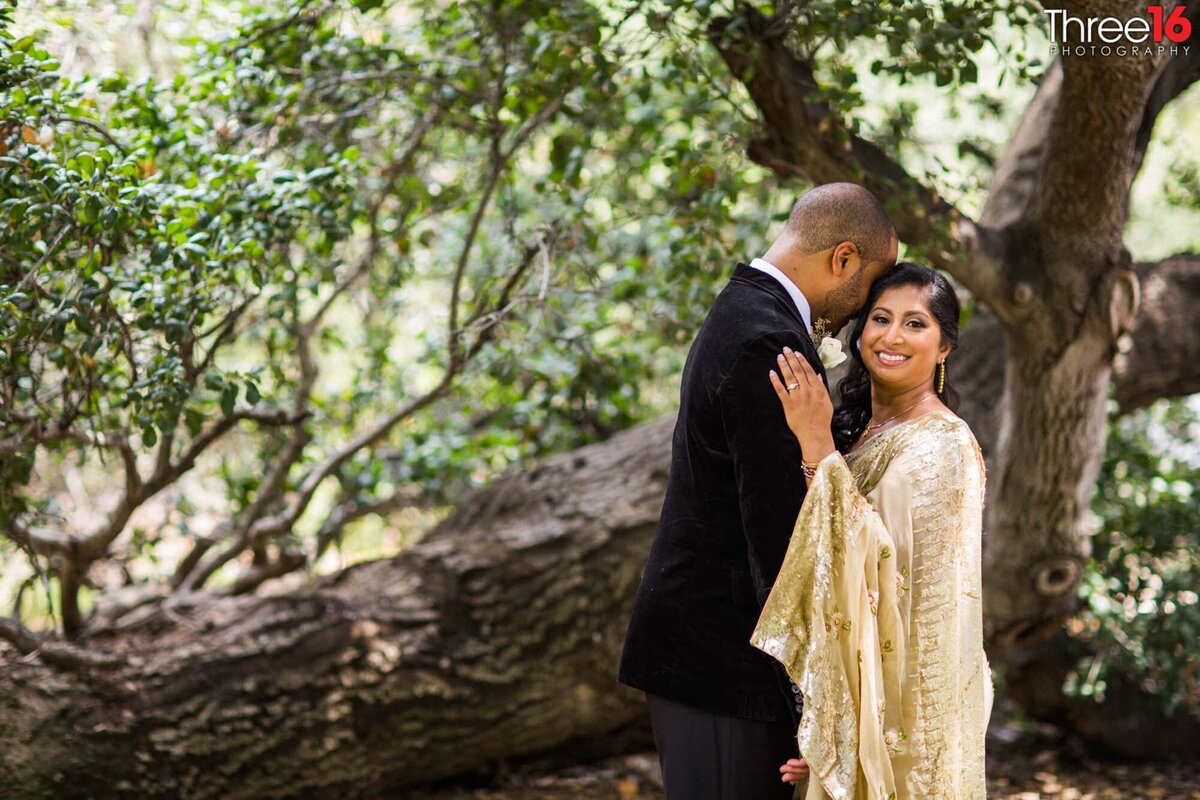 Groom embraces his Indian Bride out be a tree as she smiles for the camera