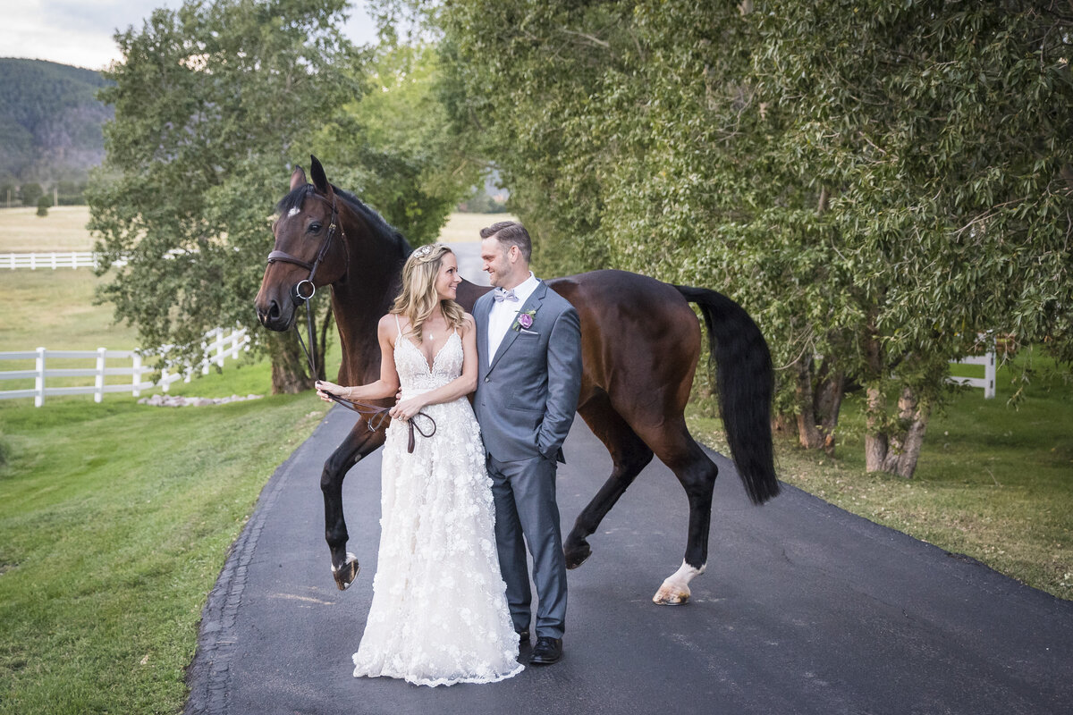 A bride and groom look into each other's eyes as the bride holds the lasso of her horse in the background.