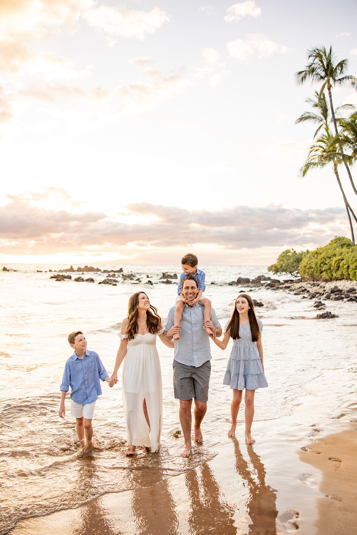 Maui Family Photographers capture father holding child on shoulders with family walking alongside during family beach photos