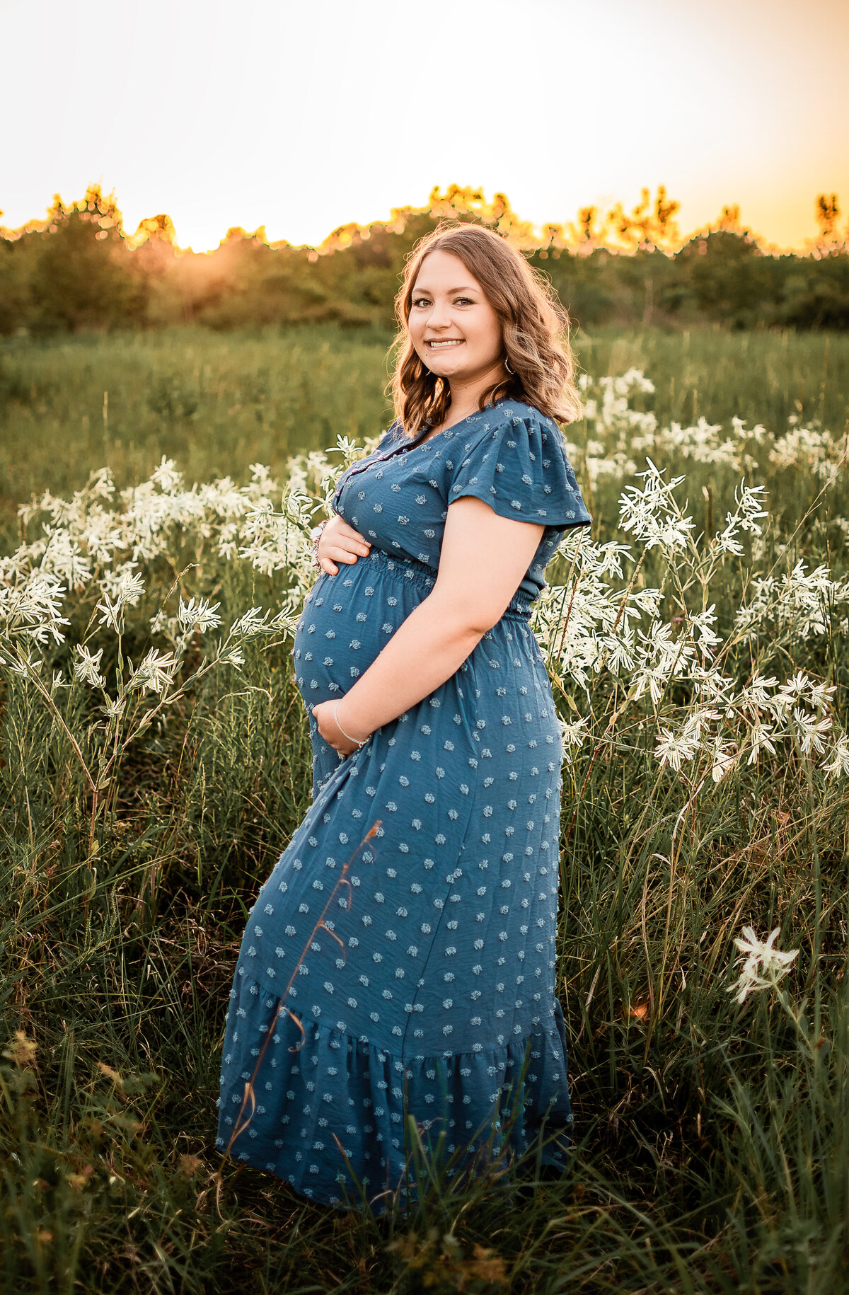 A Houston expectant woman holds the top and bottom of her belly as she smiles at the camera.