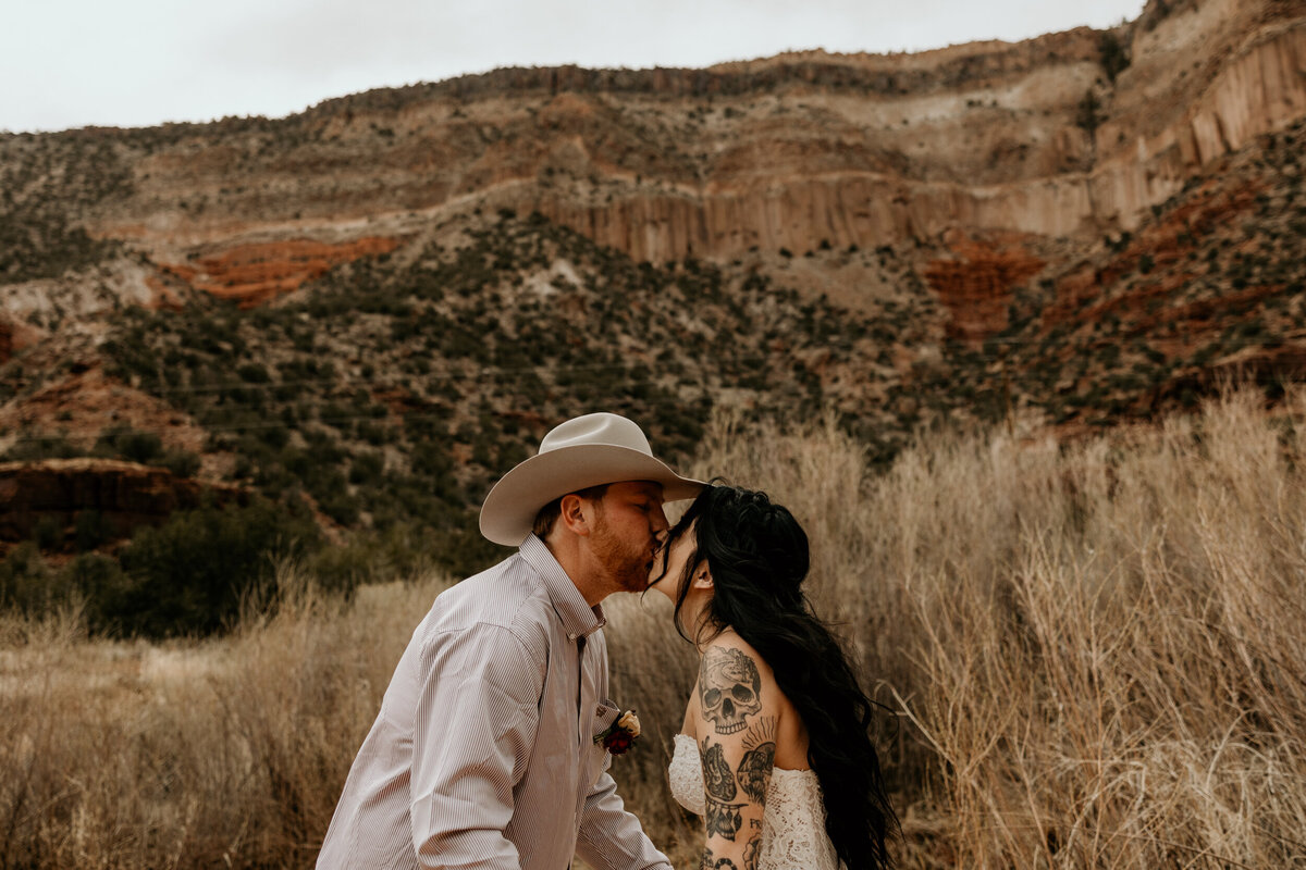bride and grooms first kiss in front of Jemez Springs red rocks