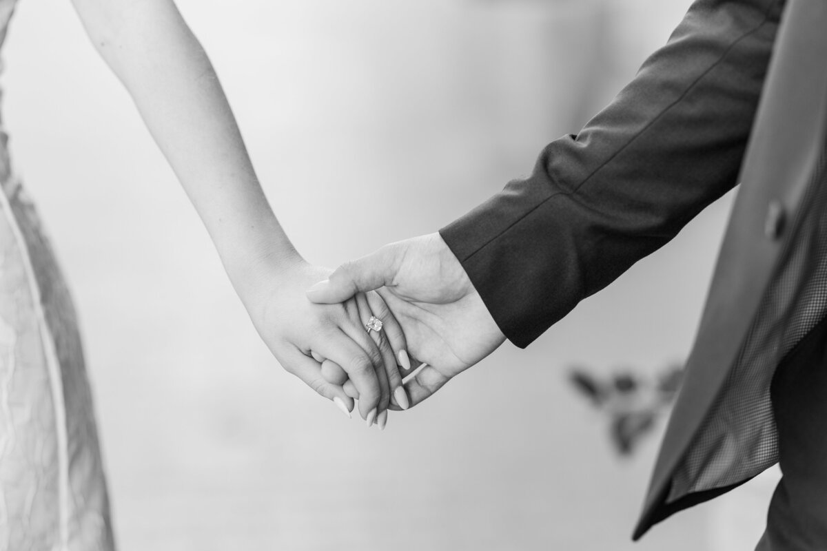 Elegant black and white image capturing a close-up of a couple holding hands, highlighting a radiant engagement ring. A classic and romantic moment from a downtown Fort Worth engagement session.