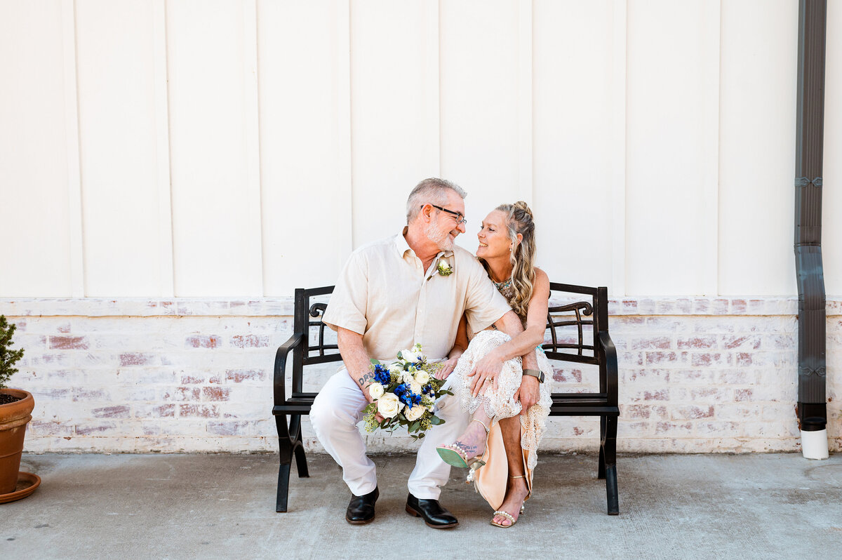 Bride and groom smiling at each other sitting on a bench