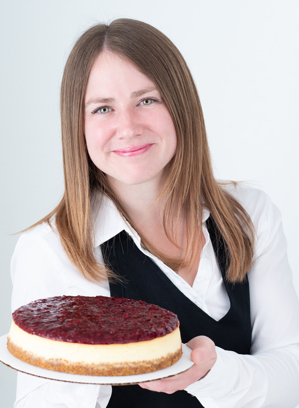 closeup image of a baker in her chef uniform holding a cheesecake