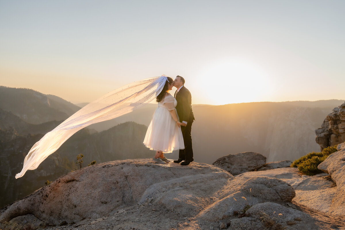 Bride and Groom eloping at Yosemite National Park Taft Point with golden sunset and flying wedding veil shot.