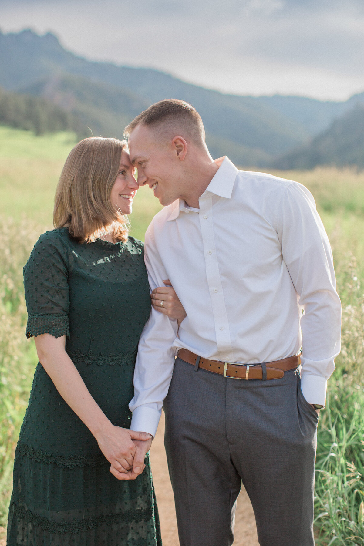 The woman in a lacy green dress touches her forehead to her fiance as she displays her new engagement ring