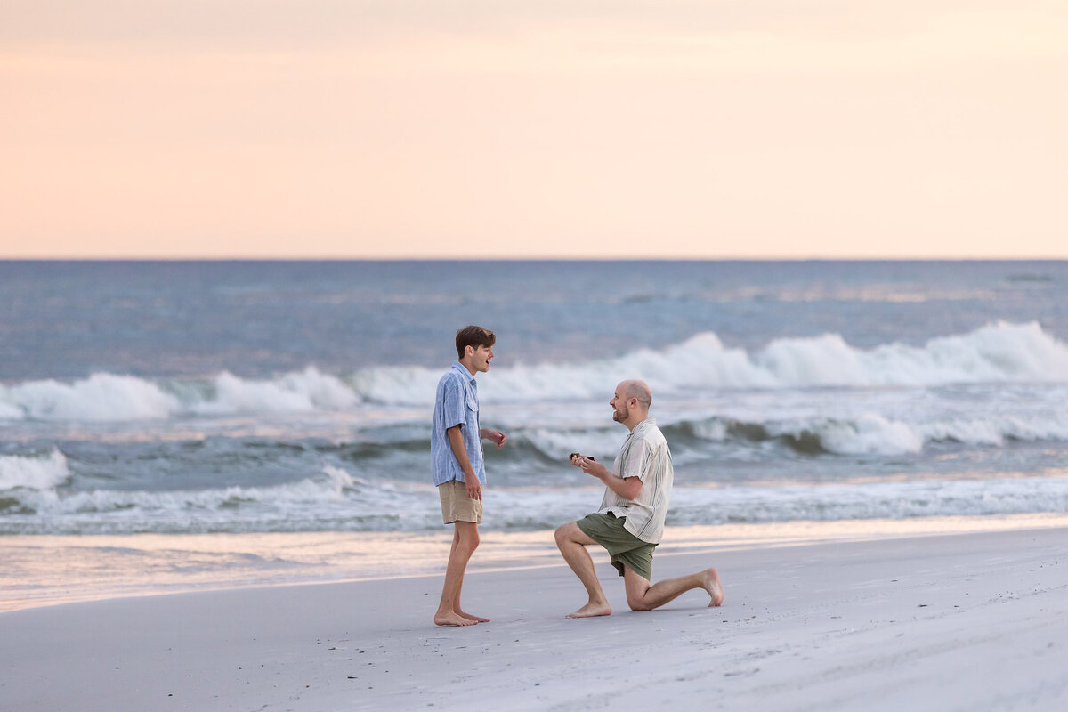 Man is kneeling proposing to his boyfriend on the beach at Deer Lake State Park, Florida.