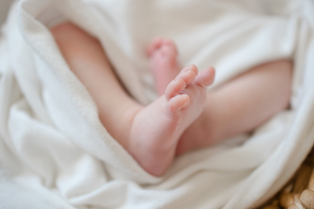 newborn feet are nestled in white blankets in this newborn portrait in minneapolis, mn