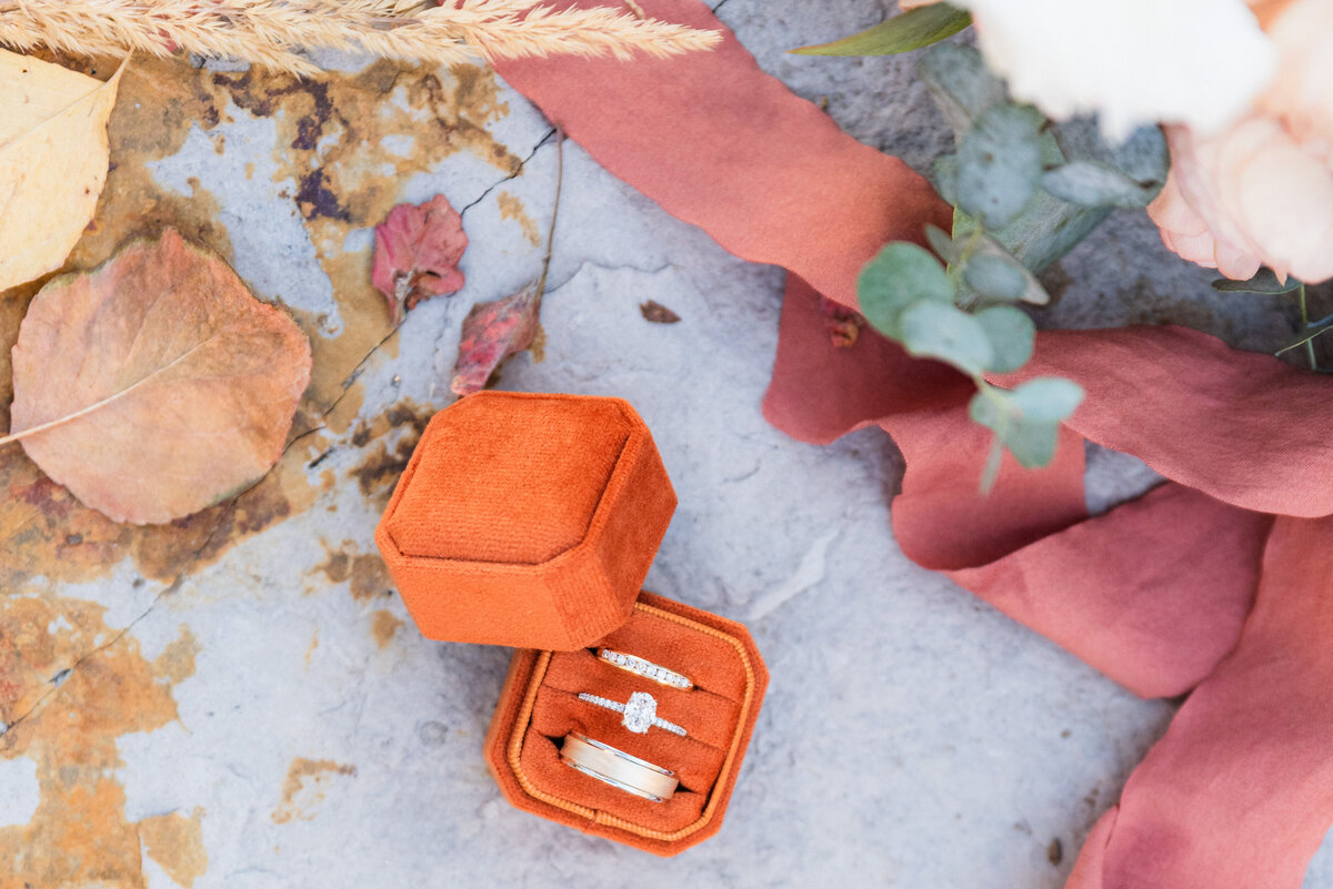 A diamond ring and man and woman's wedding bands are in a burnt orange velvet ring box/