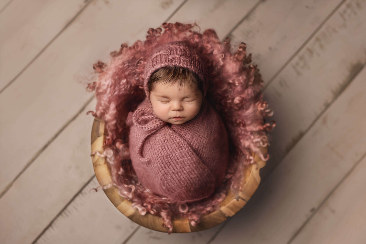 Newborn girl sleeping in bowl and swaddled in pink