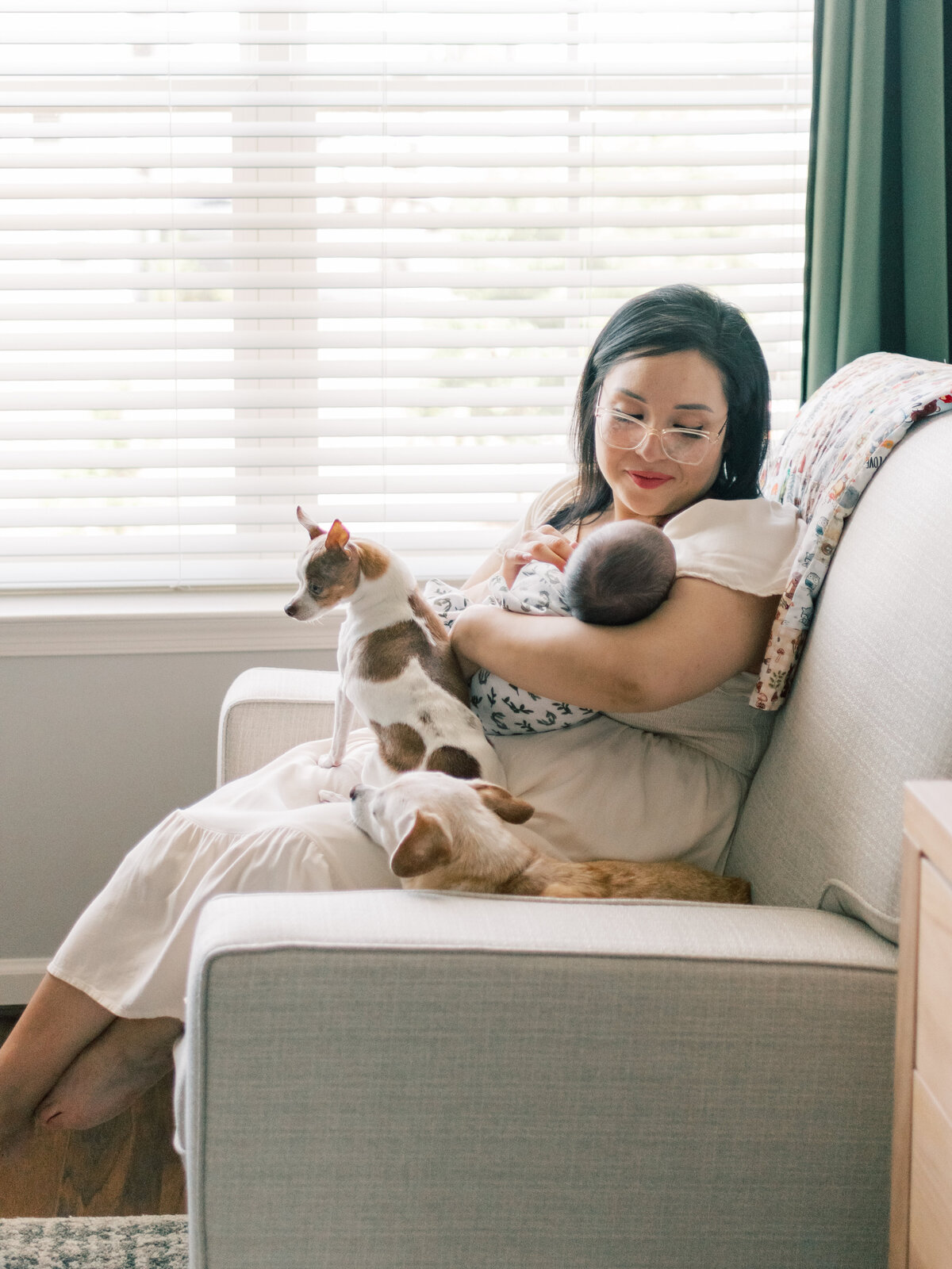Mom holding her newborn son with dogs sitting in rocking chair in Richmond baby room.