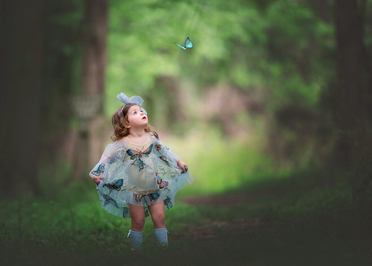 Girl in blue butterfly dress looking at a blue butterfly in the air - Los Angeles Children’s Photographer