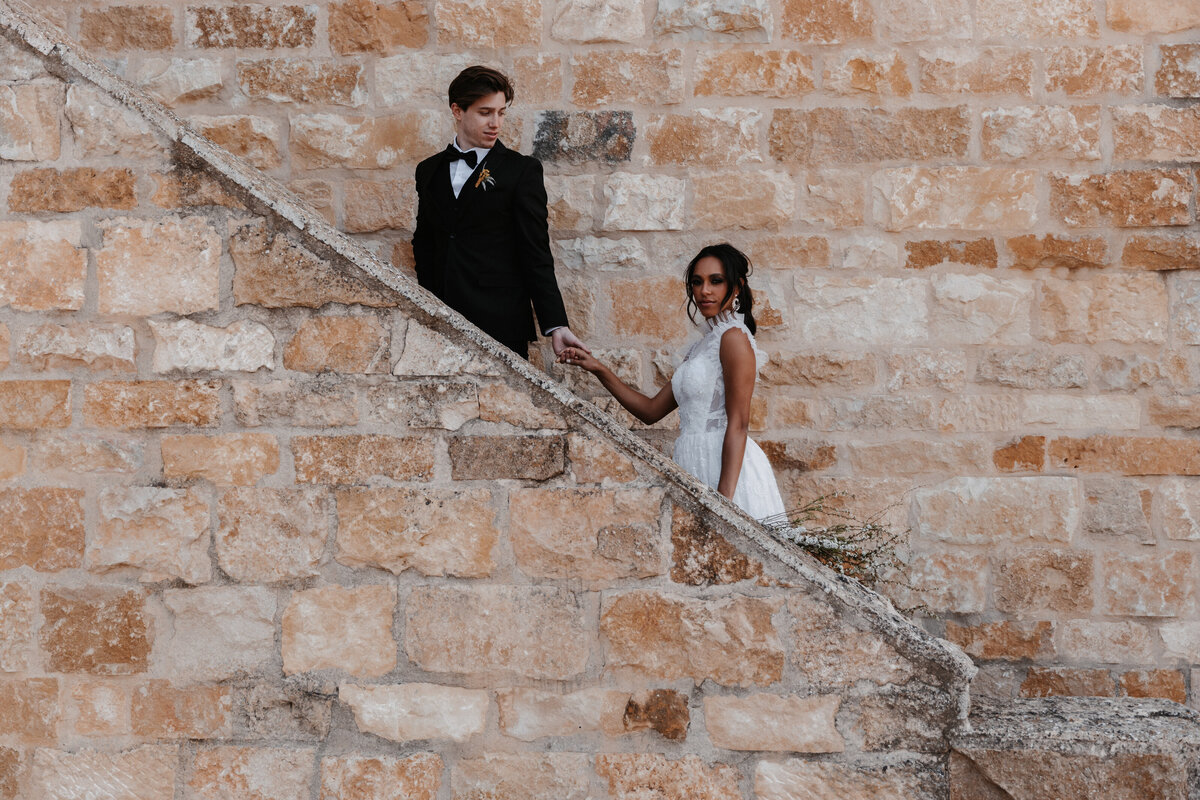 Bride and groom hold hands while standing on a rustic stone staircase at Sunstone Winery.