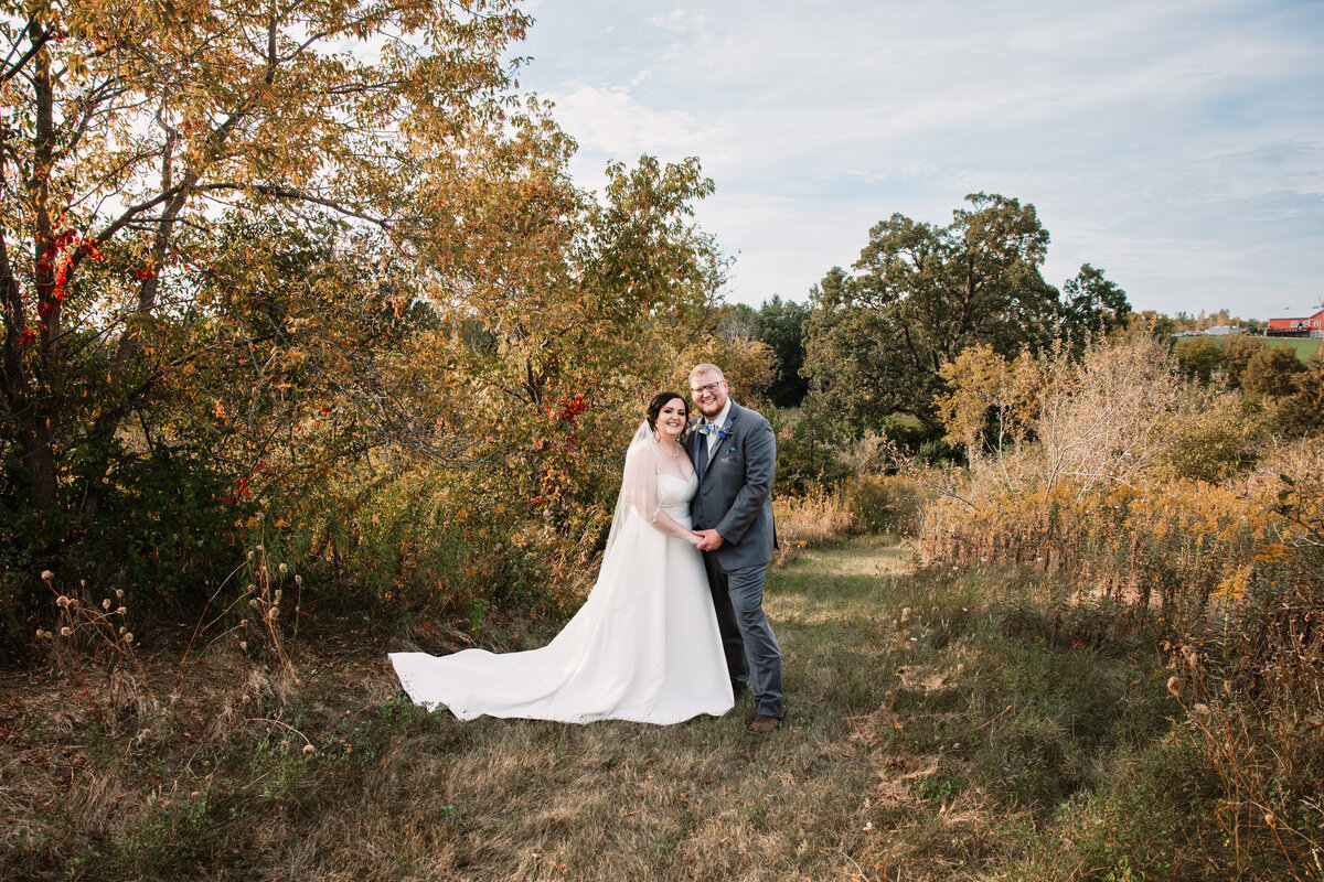 A bride and groom snuggle while walking in a trail holding hands