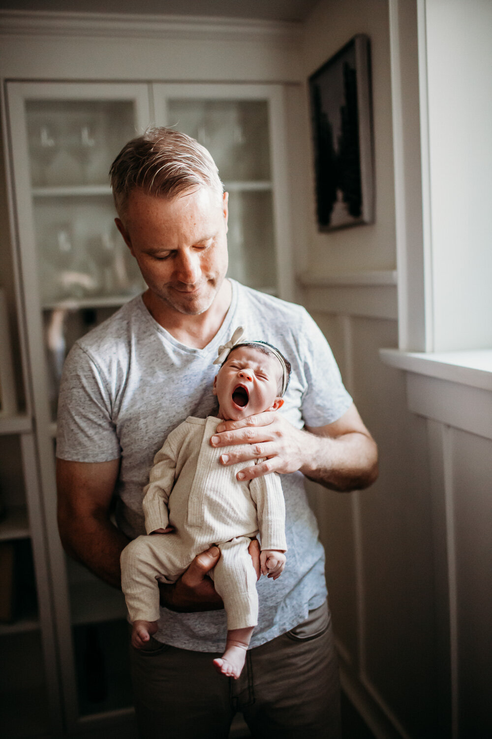 dad holding yawning baby girl during in home toronto newborn photography session