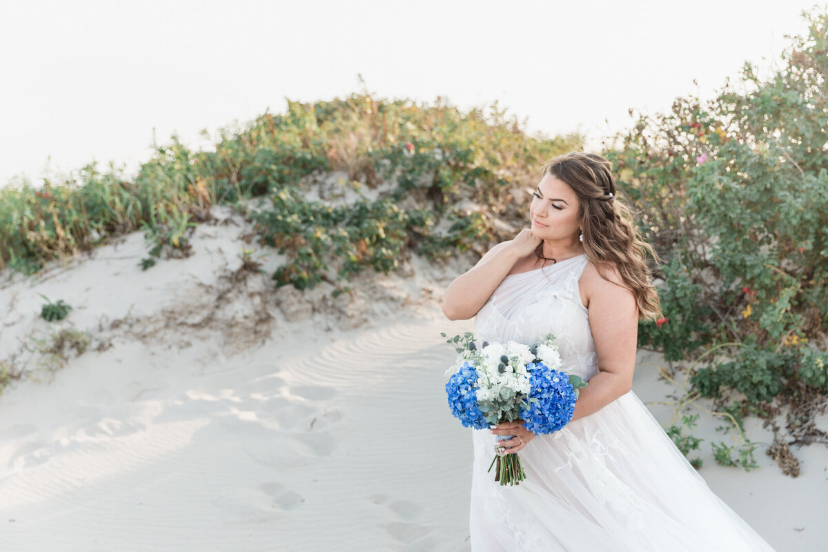 Bride in a  flowing wedding dress with a white and blue bouquet on Cape Cod