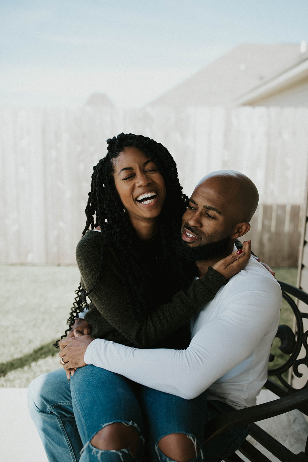 Couple outdoors, the woman laughing with her eyes closed, embraced by the man.