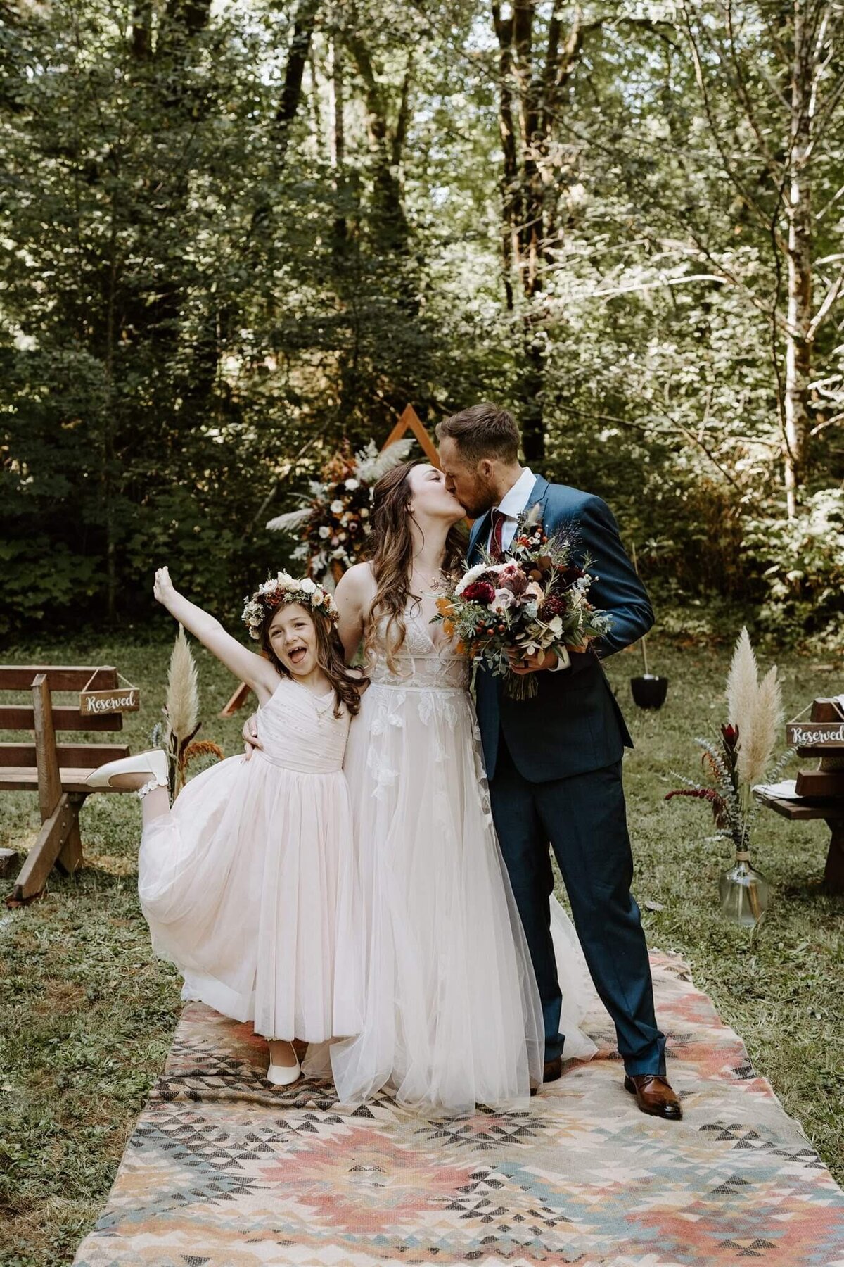 Bride and groom kiss and their flower girl wears a floral crown.