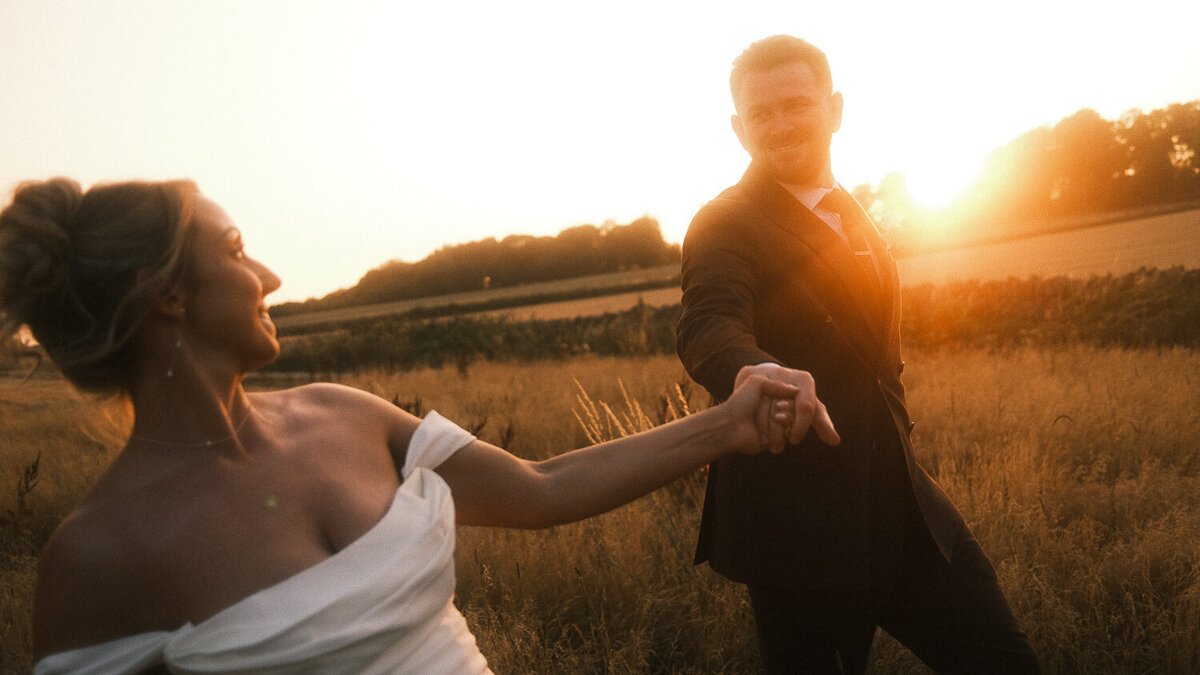 Bride and groom walk through the fields at Lapstone Barn during golden hour. 