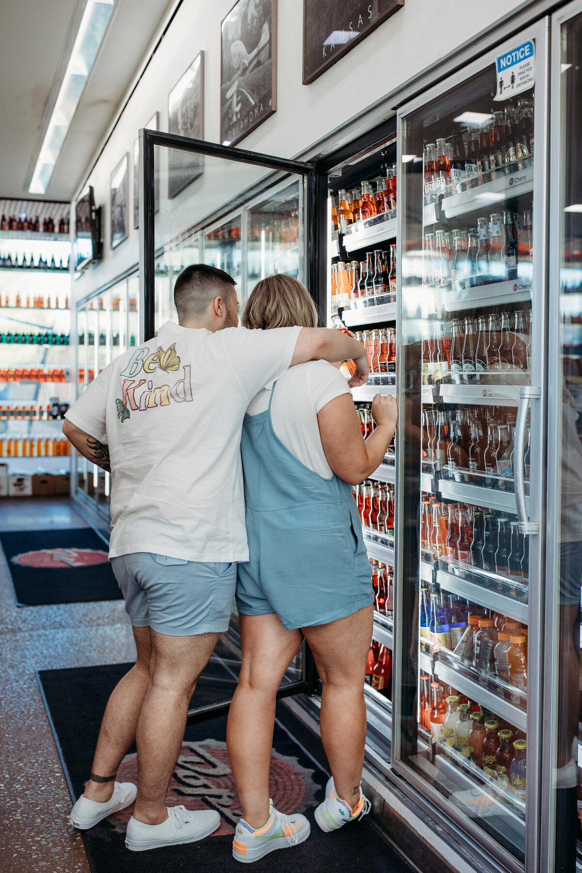 Two individuals playfully choosing drinks from a refrigerator in a convenience store