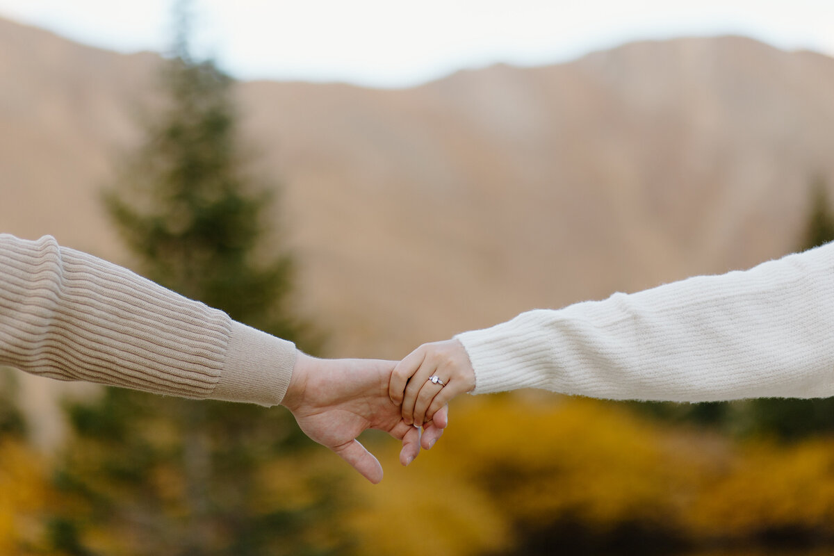 A close-up shot of an engaged couple holding hands at Loveland Pass, Colorado, during their engagement session.