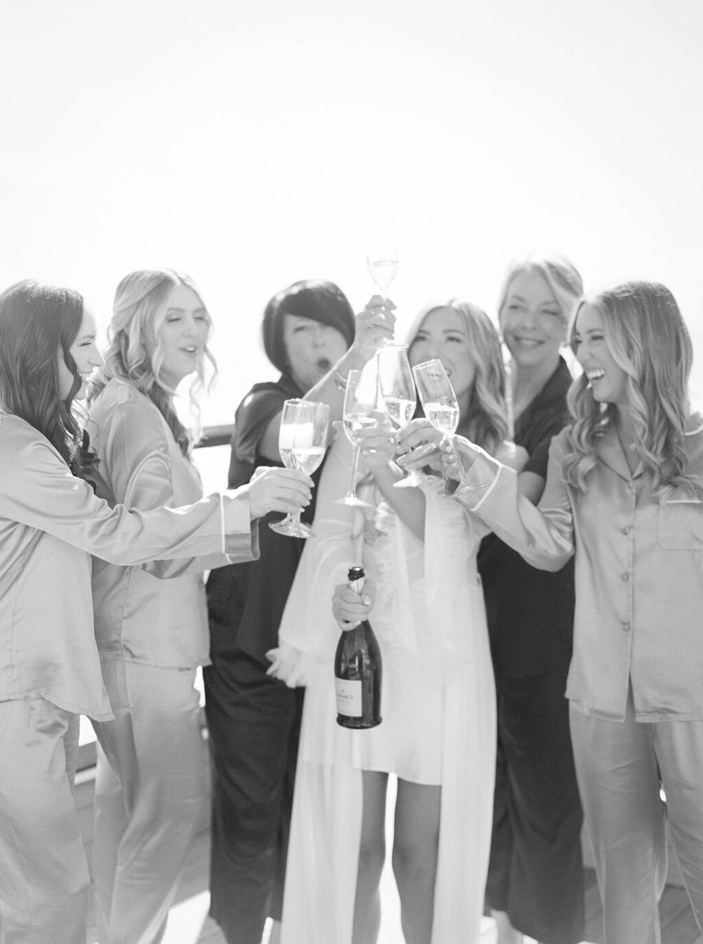 Rhode Island Wedding Photographers | A group of women in pajamas and robes joyfully toast champagne glasses. 