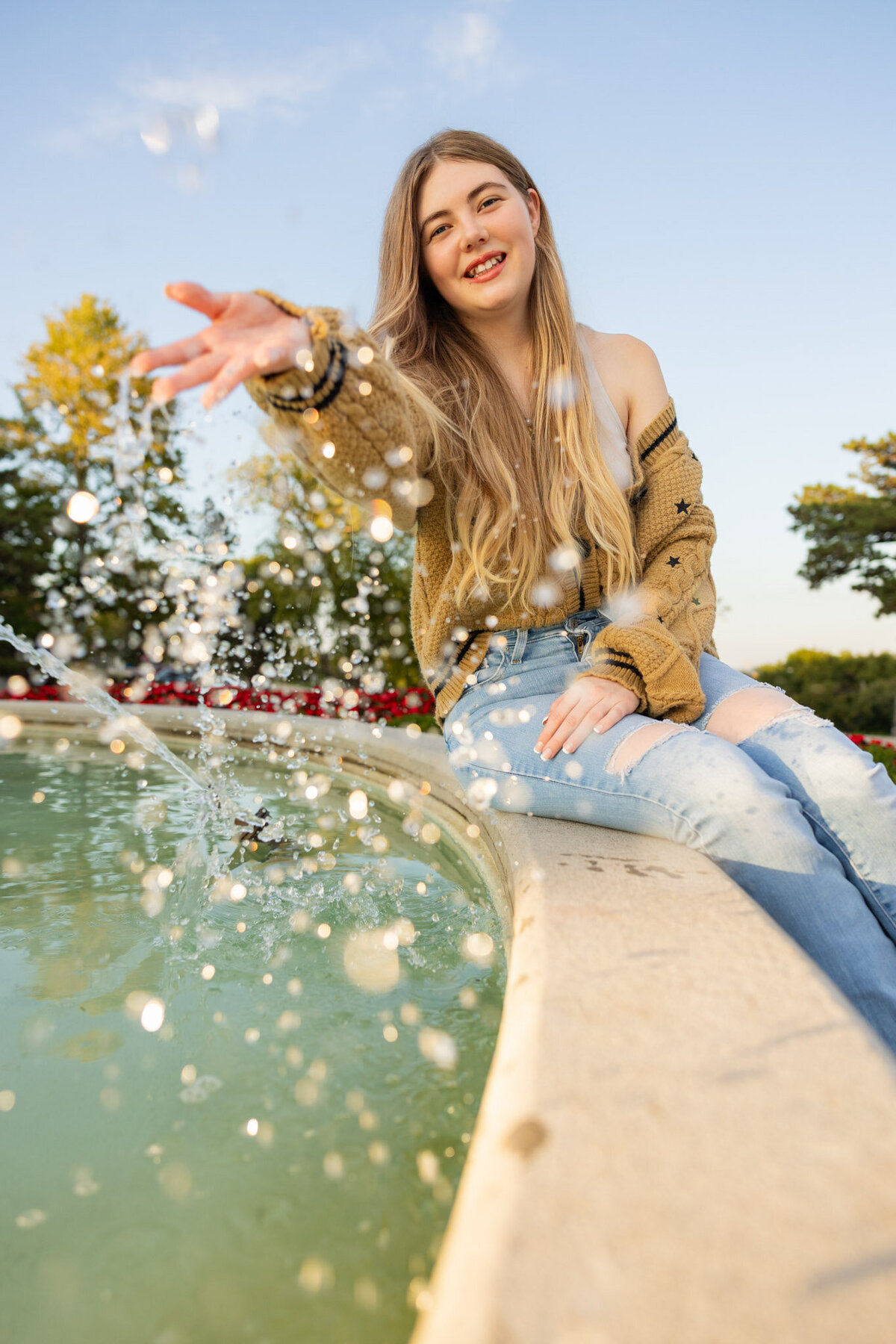 A senior girl splashing water at the camera at a fountain on the KU campus in Lawrence, KS