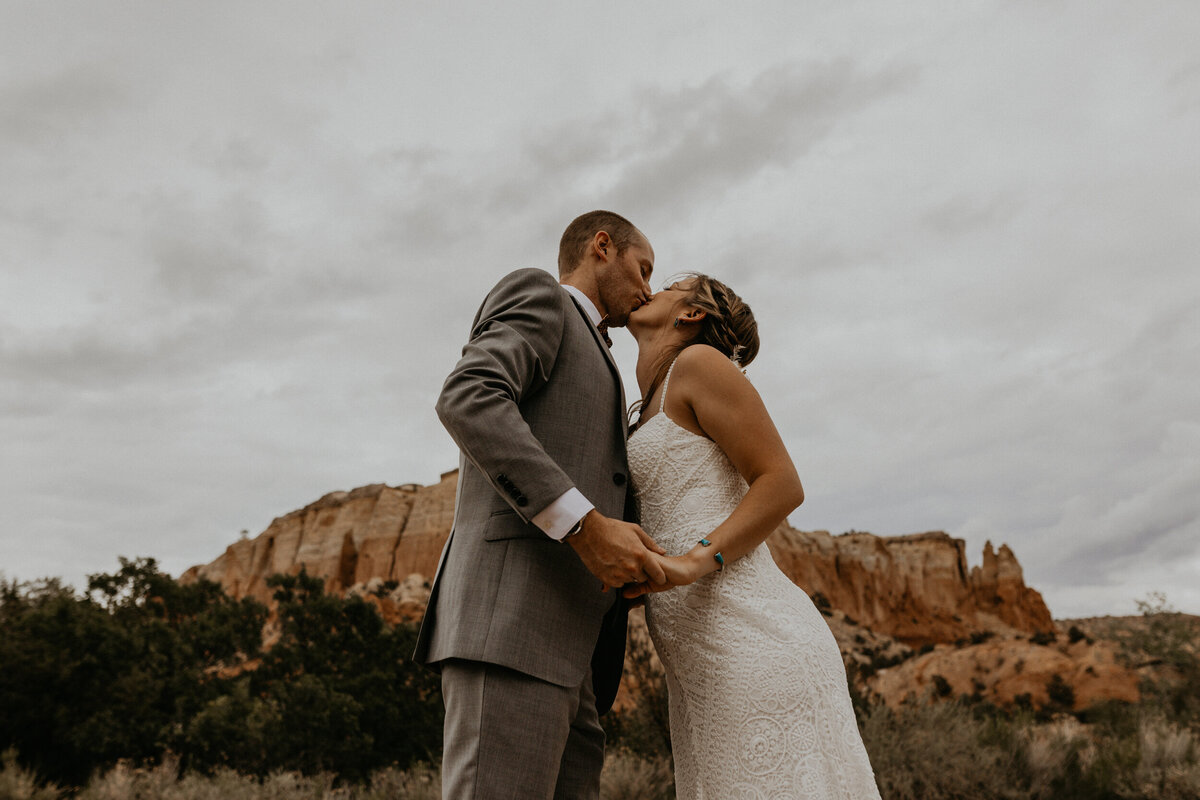 bride and groom kissing in front of red rocks at Ghost Ranch