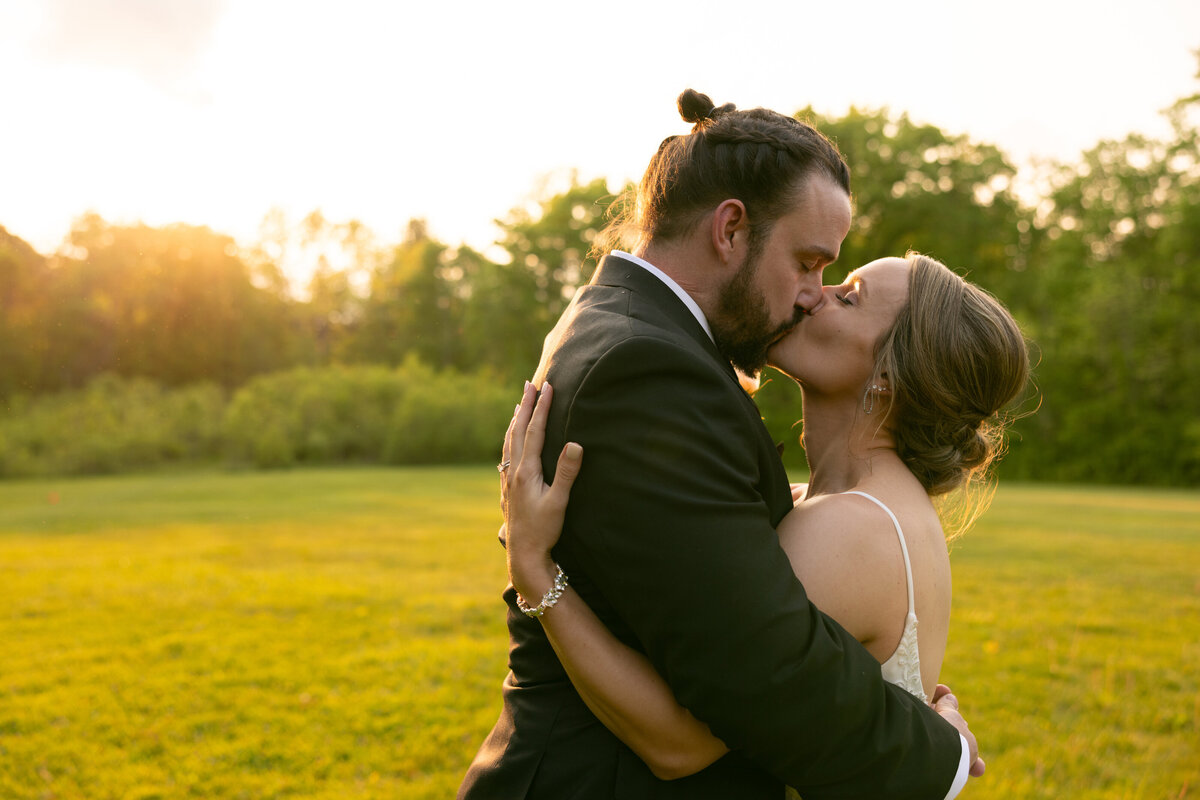 Groom and bride share a kiss during a golden hour sunset at their wedding day reception at a park in Ohio. Photographed by Aaron Aldhizer