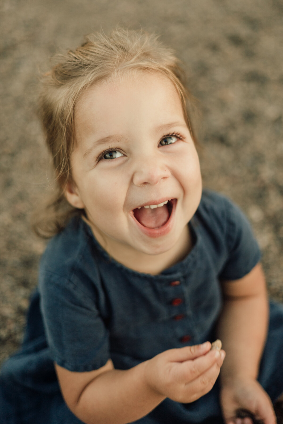 little girl looking up at the camera laughing with big smile during lifestyle family session in longmont colorado
