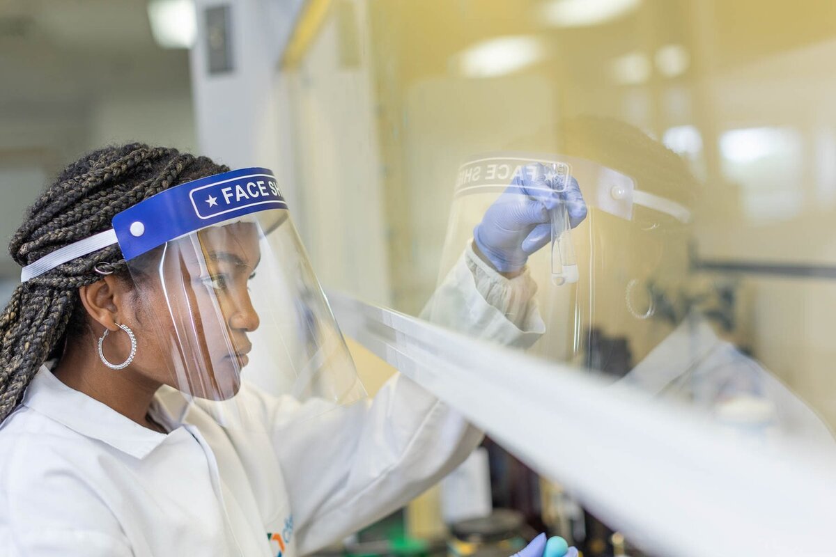 Female student with face shield looking at a test tube in a hood