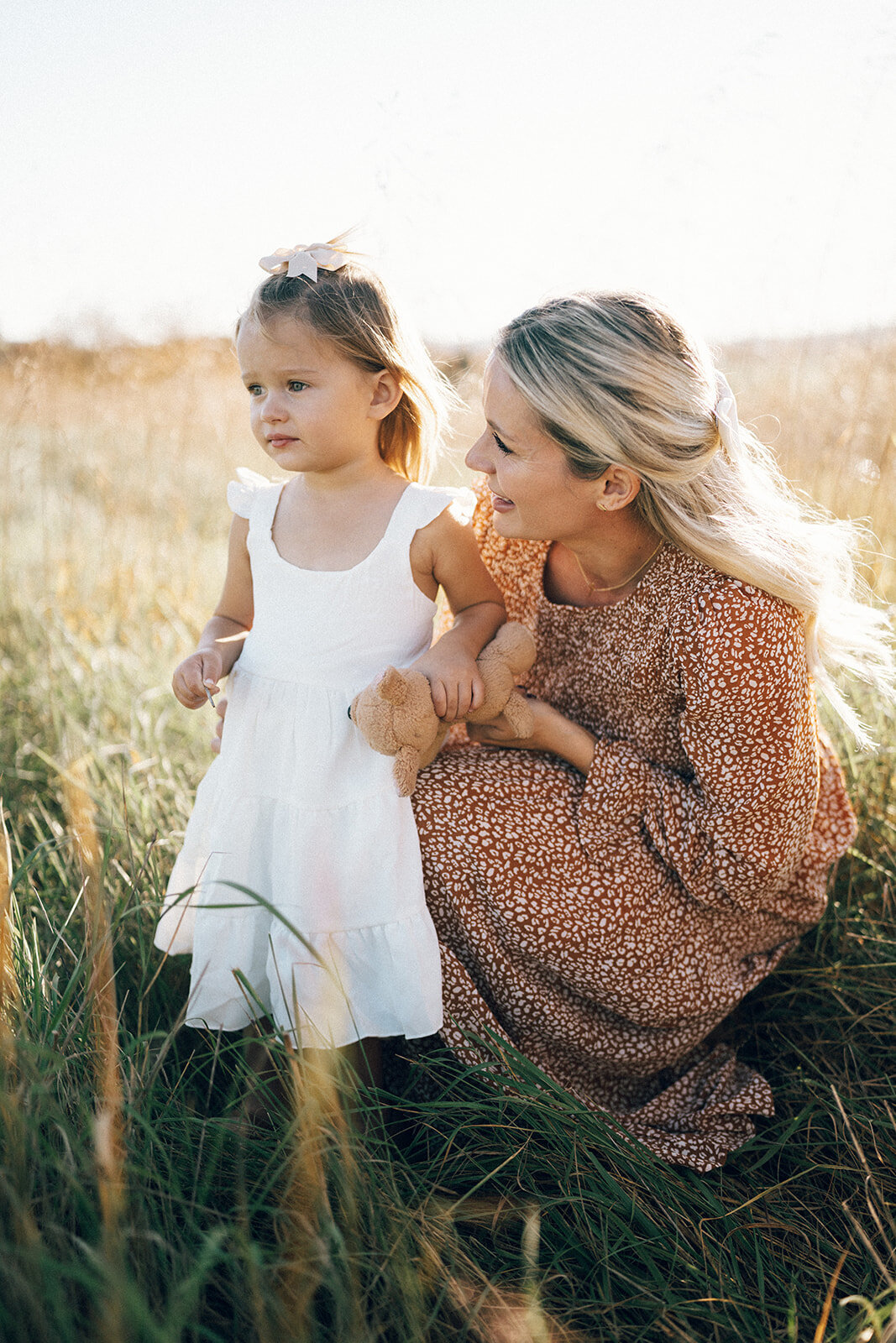Mother kneeling down to make eye contact with her daughter in a golden field during an emotive outdoor family session