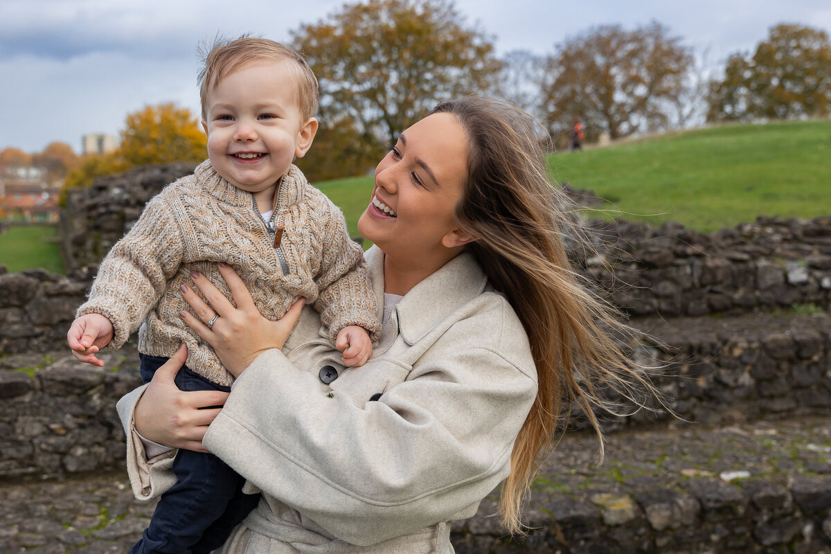 A joyful woman holding a laughing toddler in a park on a cloudy day.