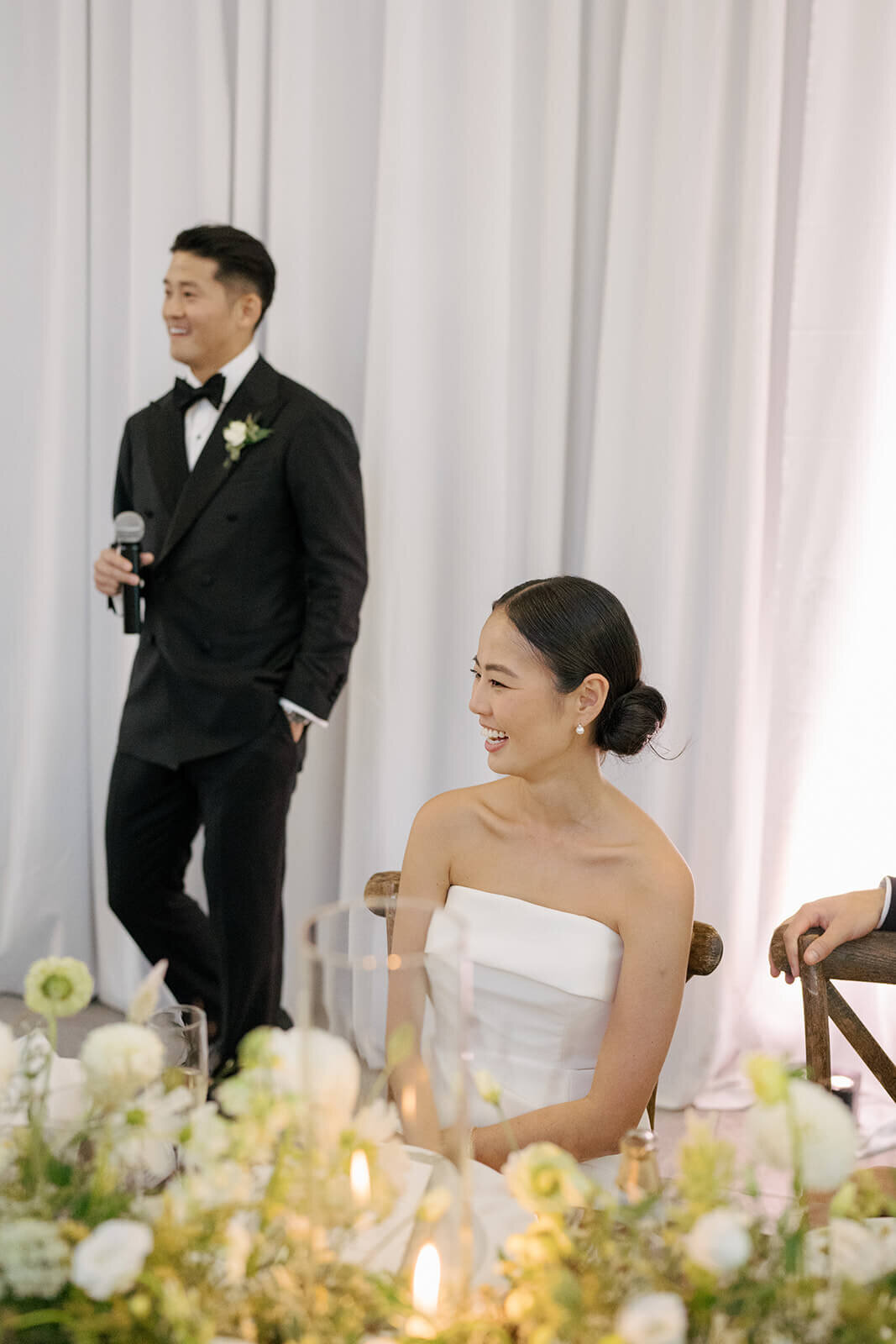 The groom stands to deliver a speech while the bride looks on during their Aspen Meadows Resort wedding reception.