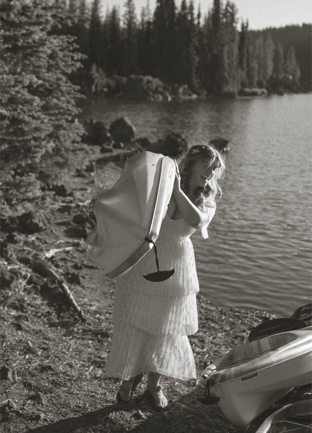 adventurous bride smiles and carries her kayak to the water at Sparks Lake in Bend, OR