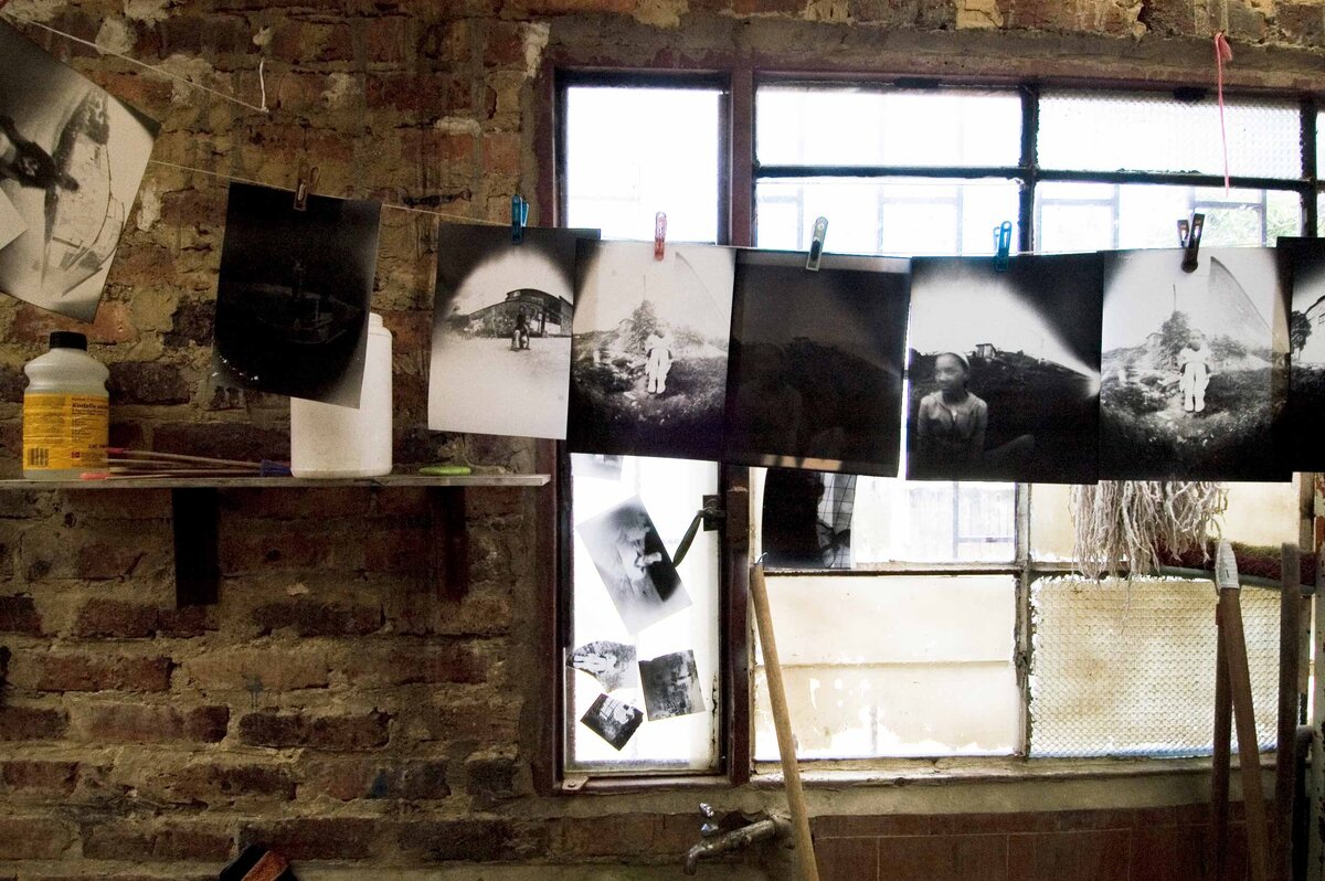 A darkroom in rural Columbia where children in the community learn photography. Black and White photos hang in front of a window with darkroom supplies in background.