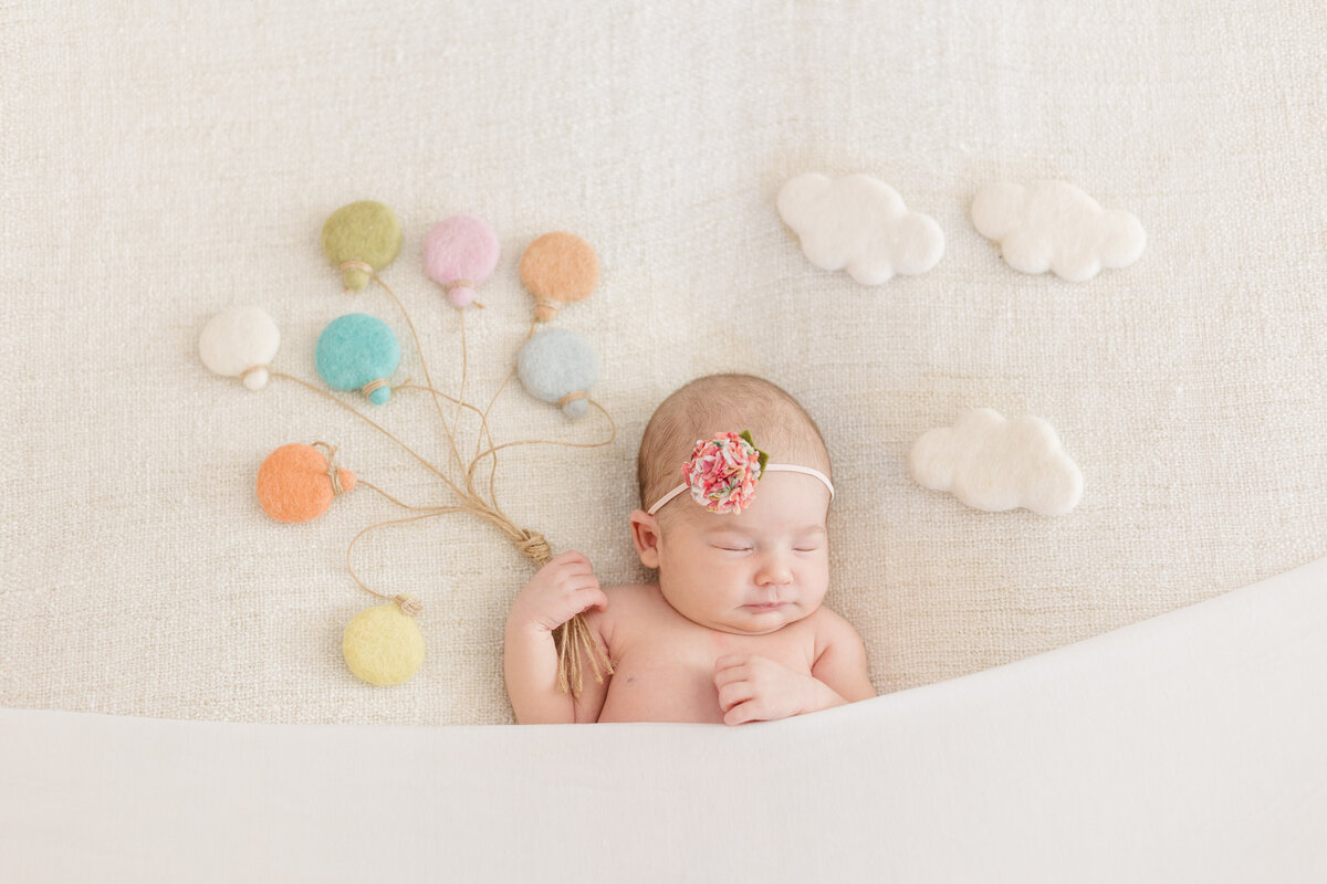 A newborn laying under a blanket with balloon and cloud shapes around them
