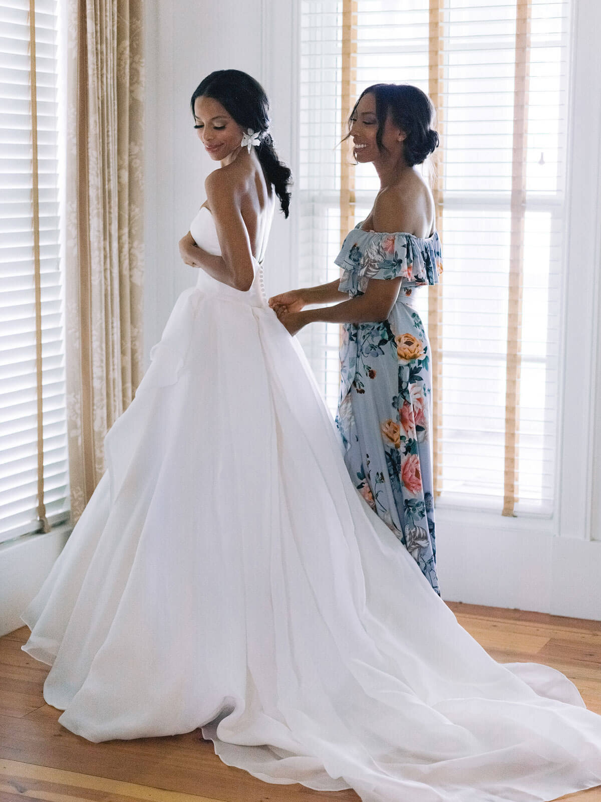 The bridesmaid is fixing the bride's gown from behind in Montage at Palmetto Bluff. Destination wedding image by Jenny Fu Studio