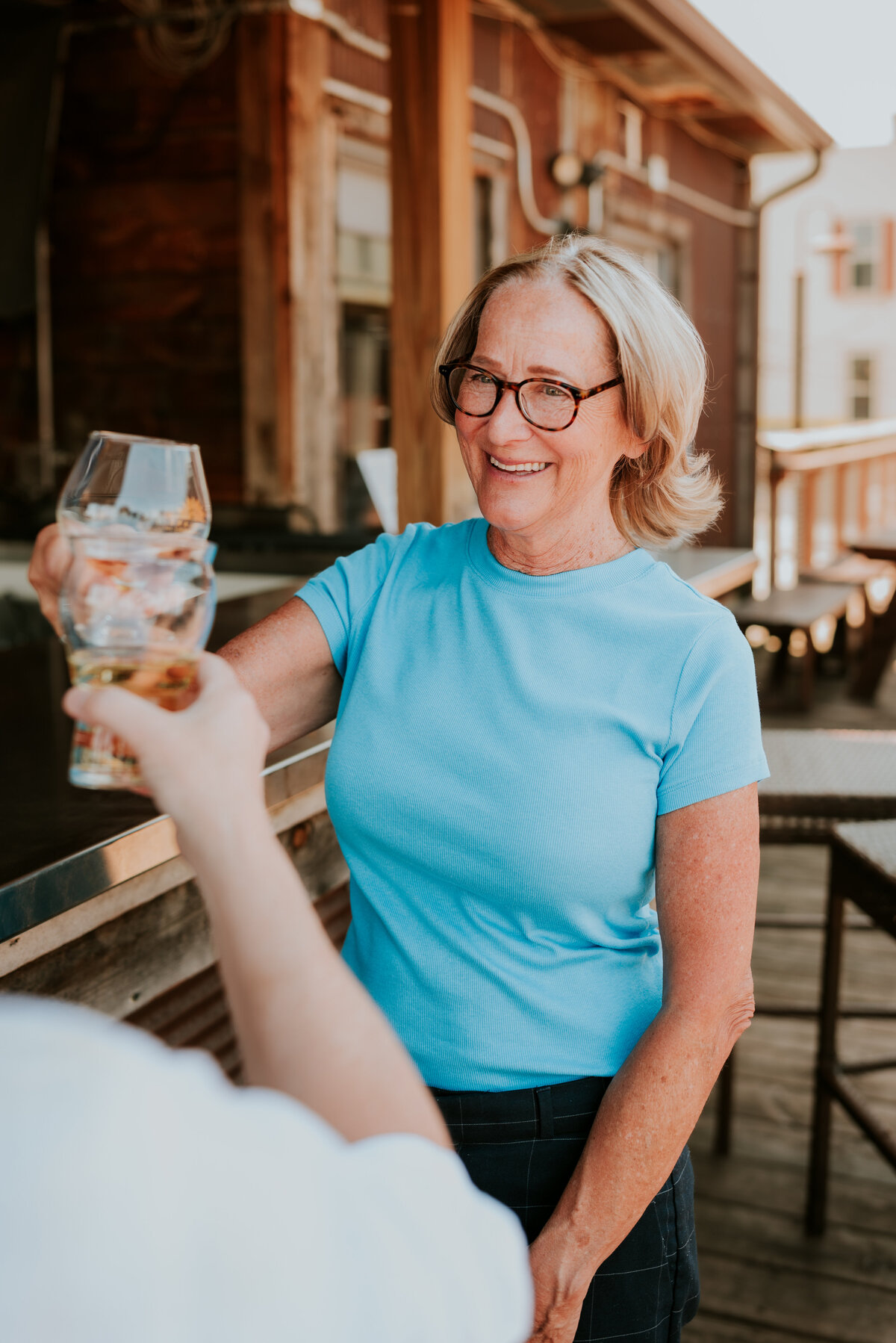 Cheerful woman in turquoise shirt raising a drink while smiling, conveying a confident and approachable vibe for dating apps.