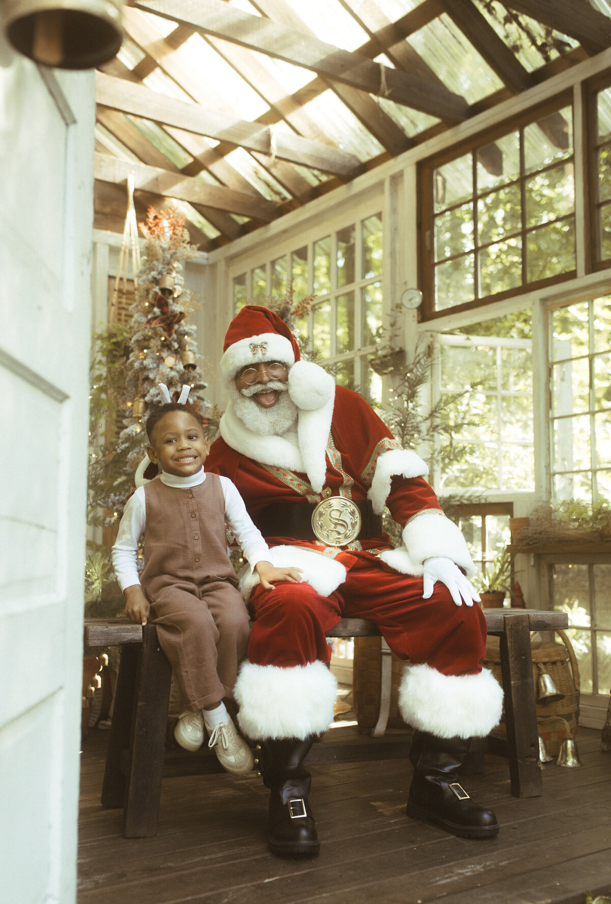A young boy sits next to The Black Santa of Atlanta with a cheesy grin. 