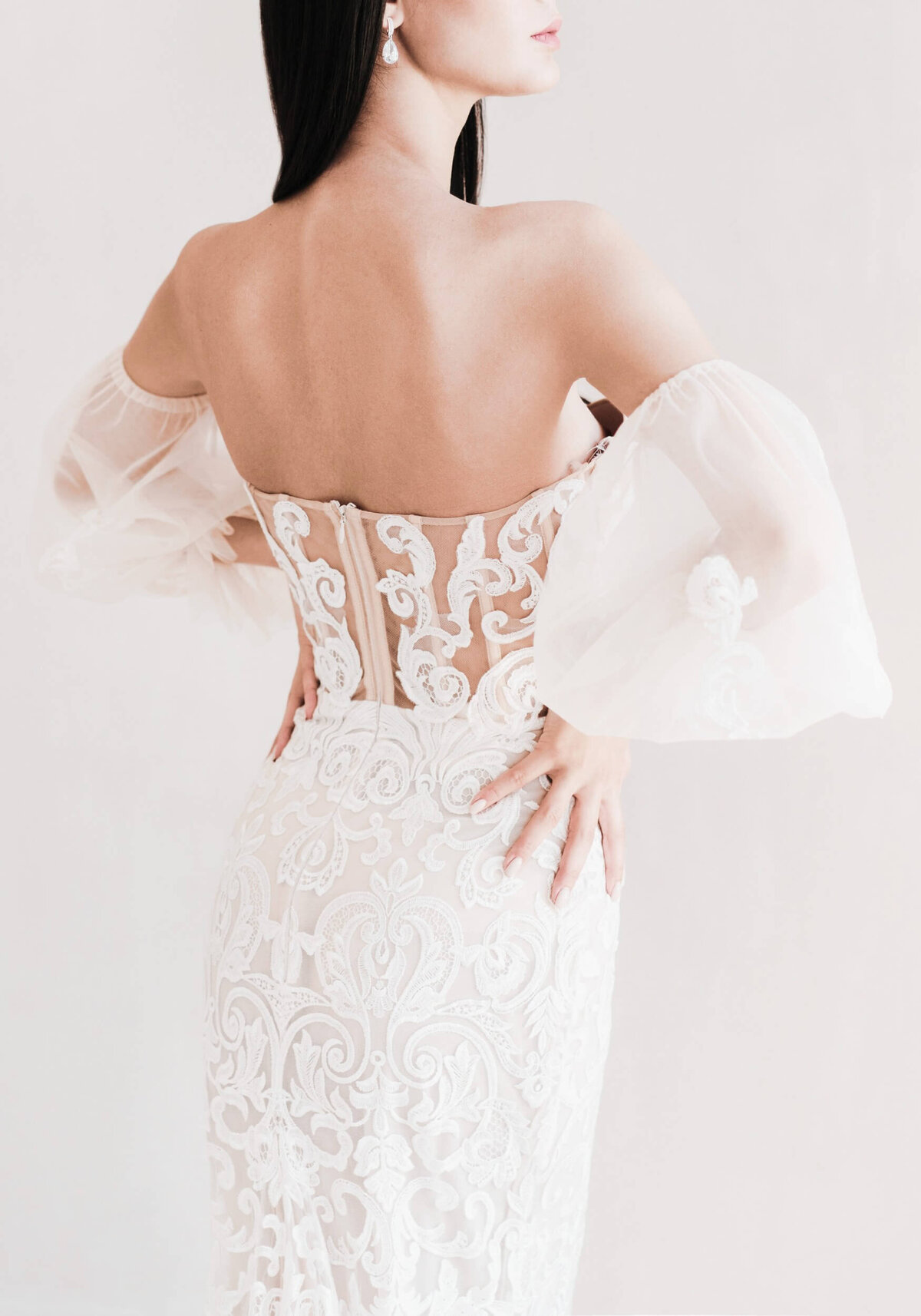 Beautiful bride dressed in the white wedding dress with the naked back. Light chiffon wedding dress with wide collapsible sleeves.