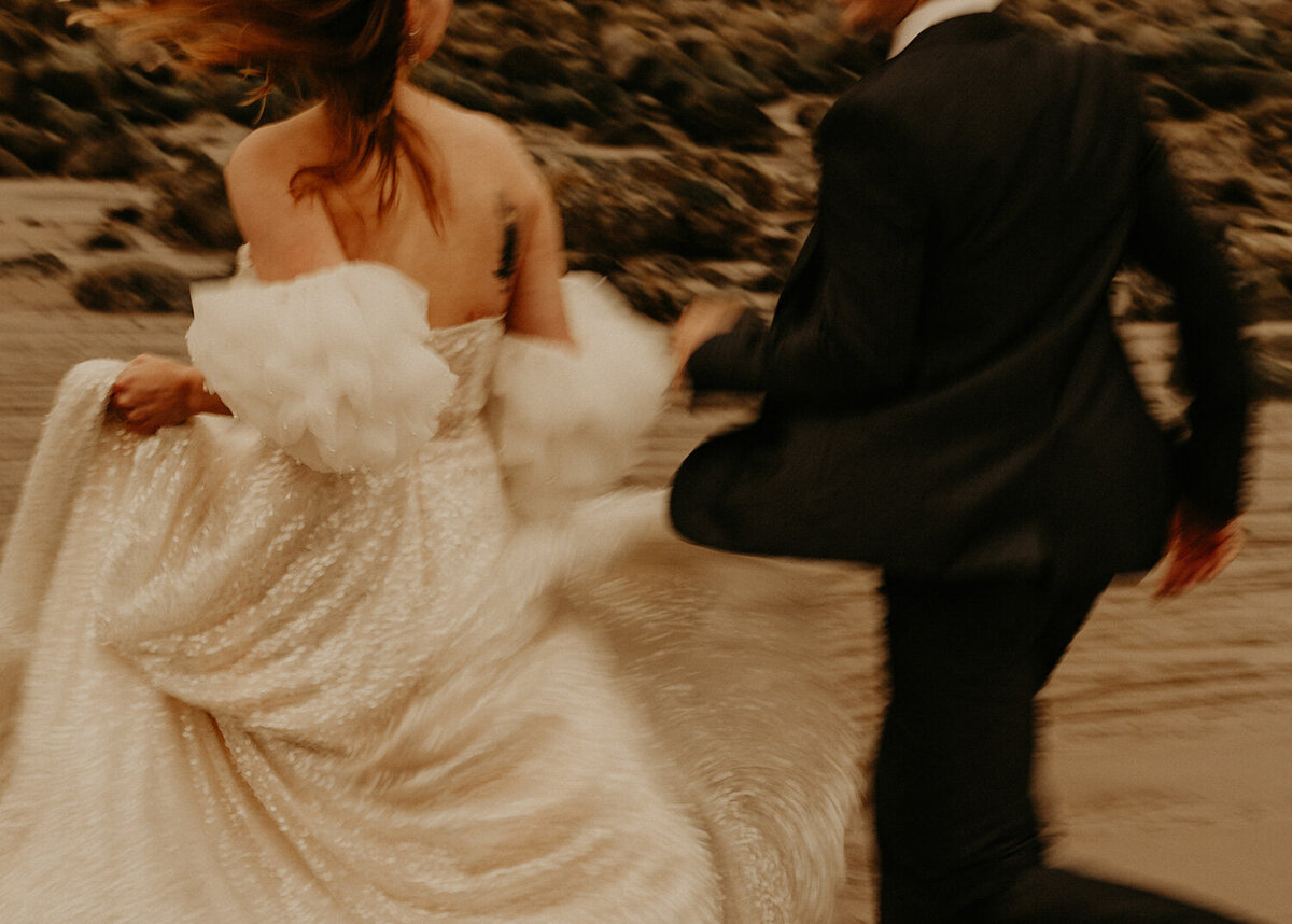 Married couple running while bride holding her gown and her husband's hand