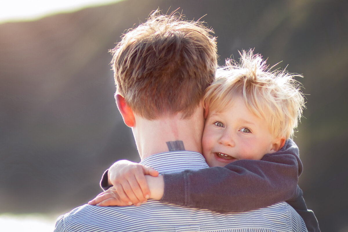 Little boy smiles over his fathers shoulder for family photo in Somerset