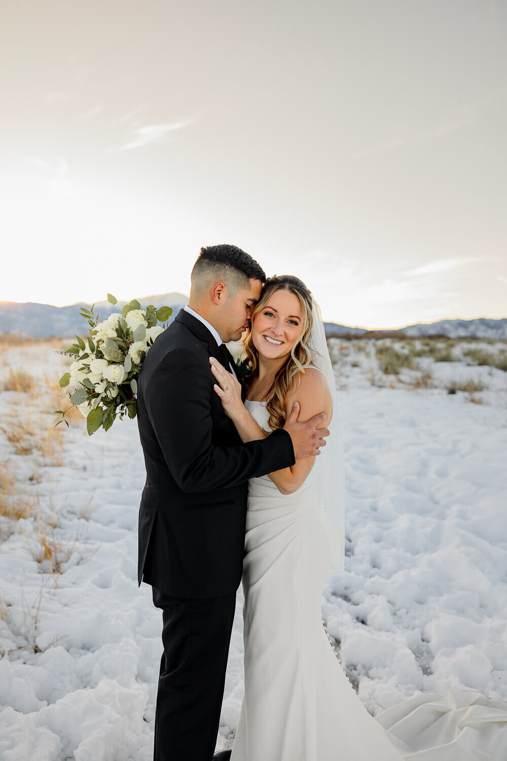 Smiling bride and groom embracing in the beautiful snow and mountains. Captured by Colorado Springs wedding photographer, Michelle Betz Photography
